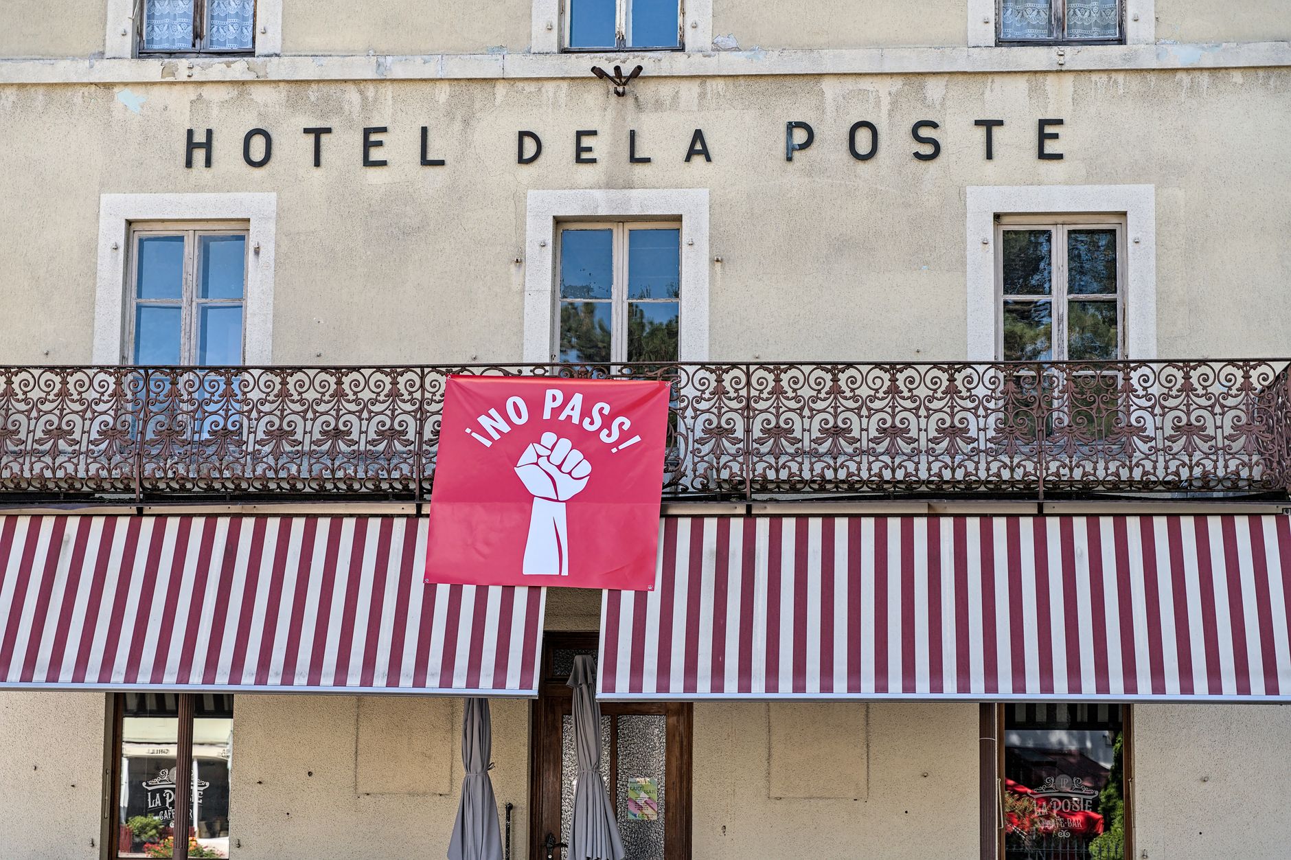 Hotel De La Poste facade with striking protest banner reading 'No Pass' in Val-de-Travers, Switzerland.
