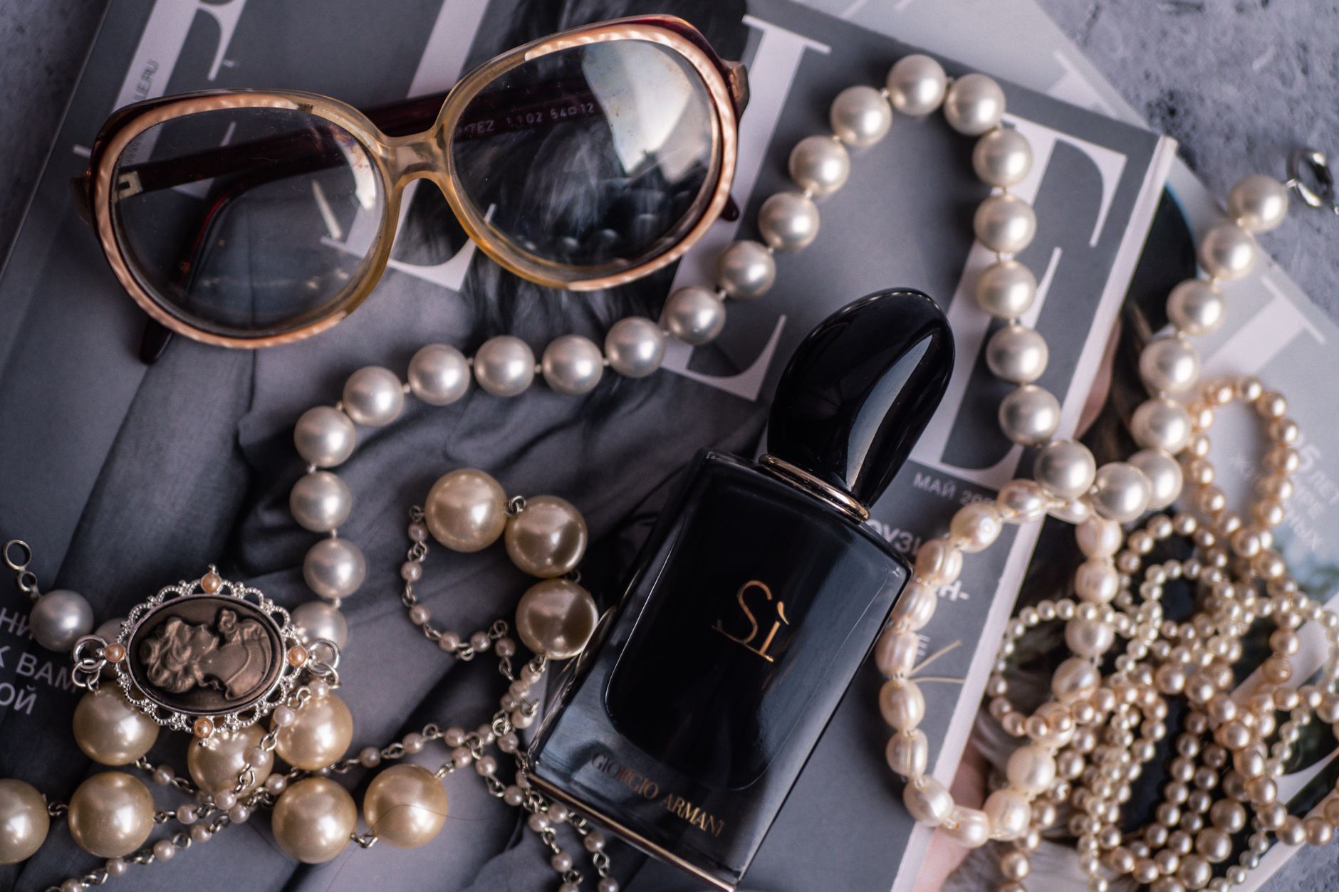 Chic arrangement of pearls, perfume, and sunglasses on a magazine.