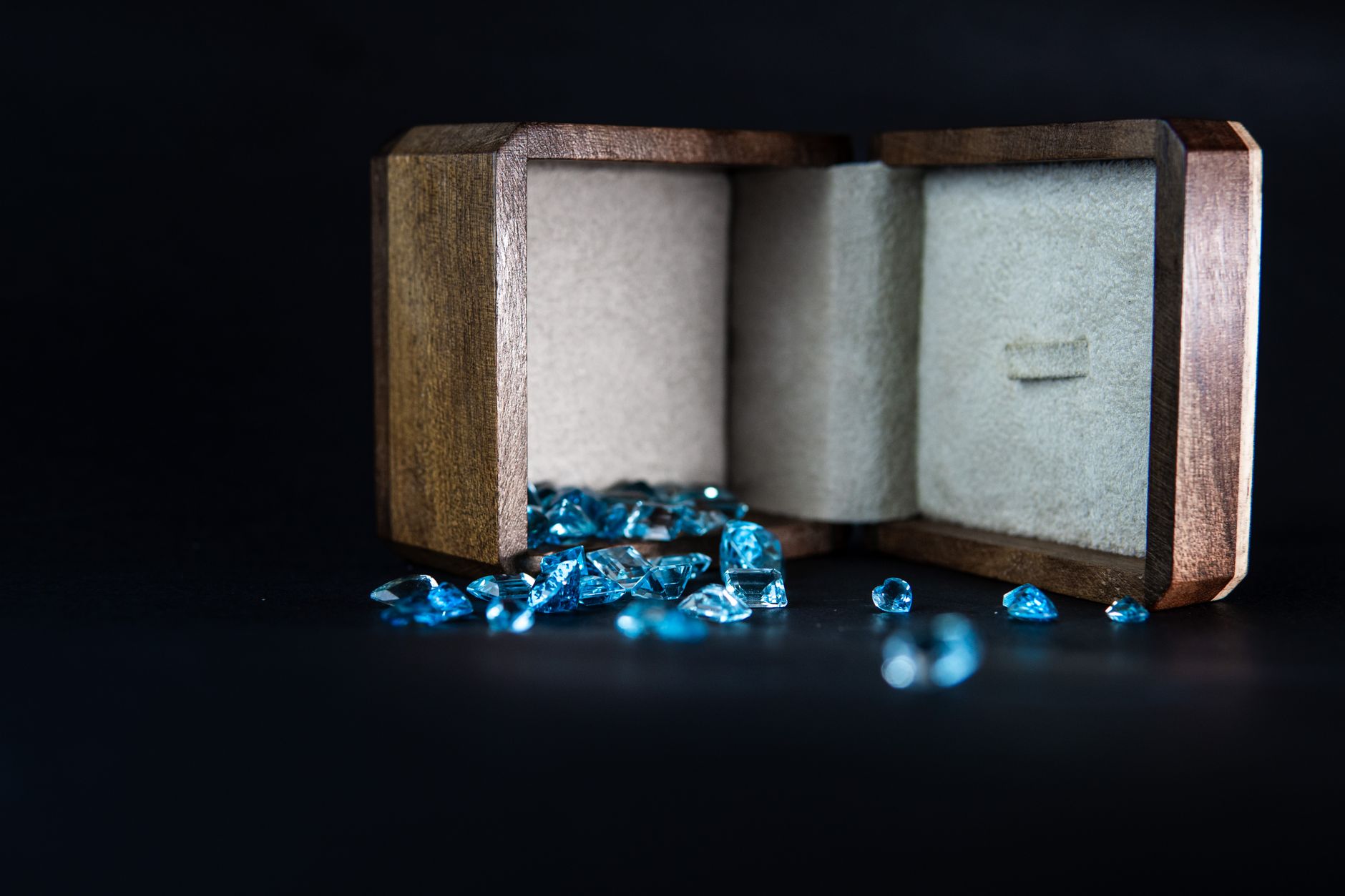 Wooden jewelry box displaying scattered blue gems, symbolizing elegance and luxury.
