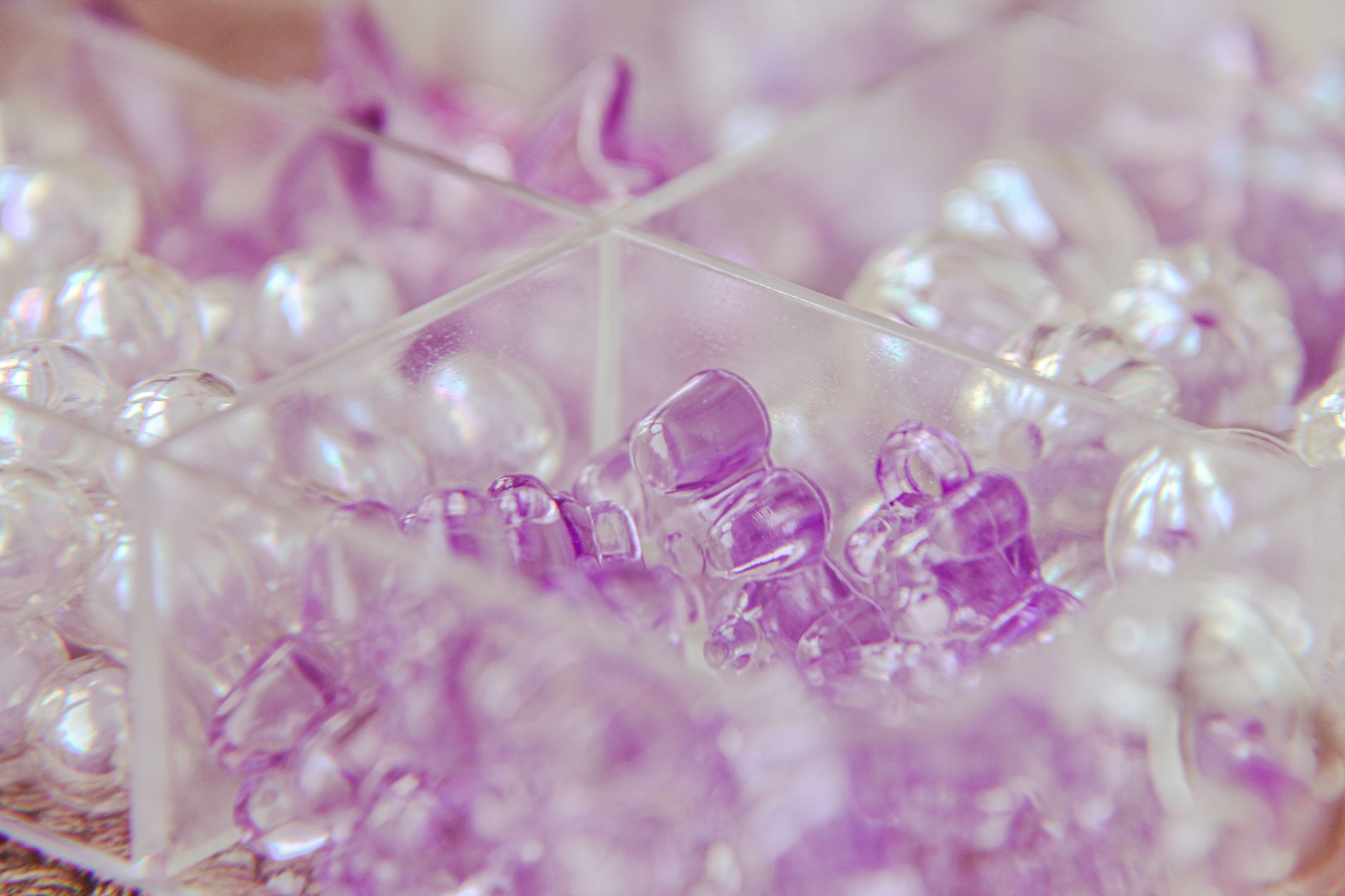 Vivid close-up of purple and clear crystal beads in a plastic container.