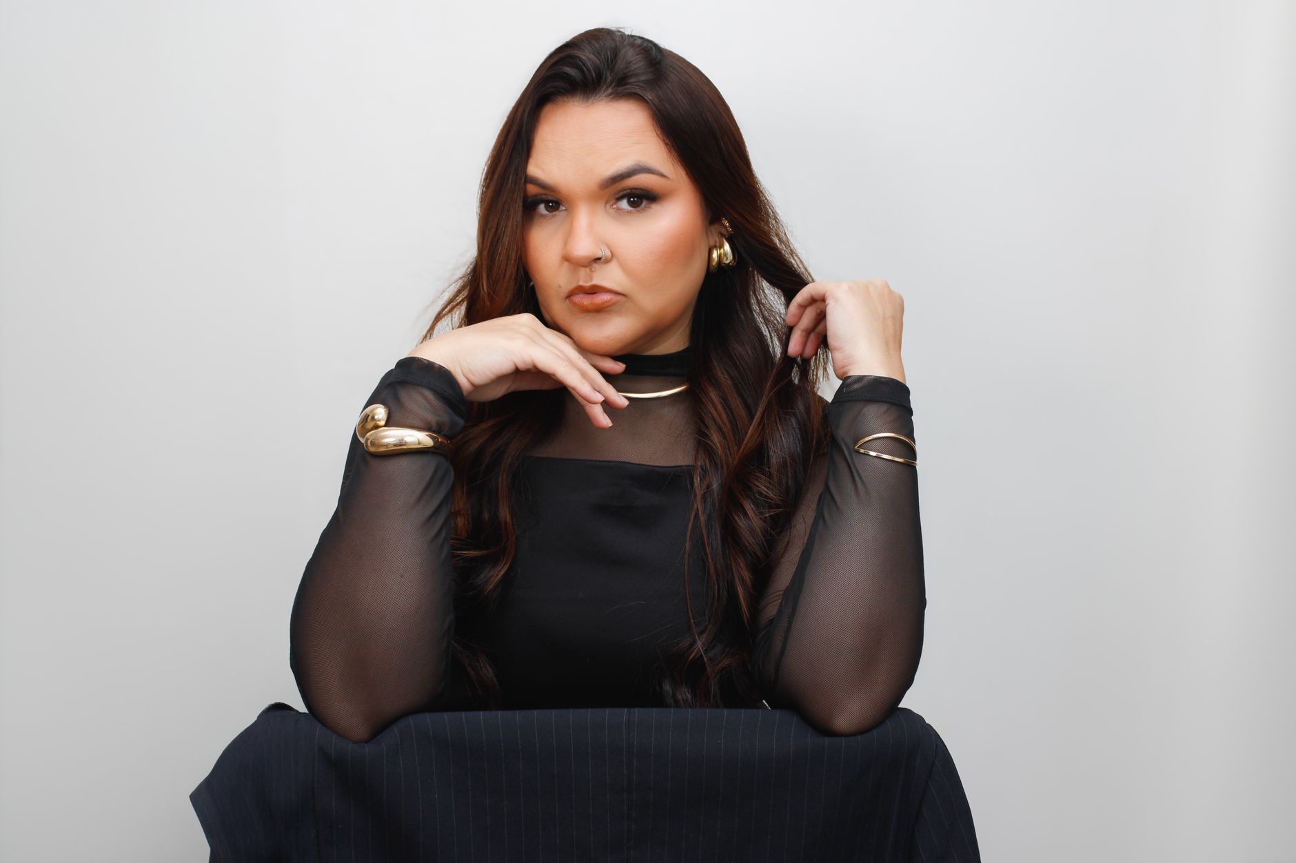 Portrait of a woman posing elegantly in black attire with gold jewelry.
