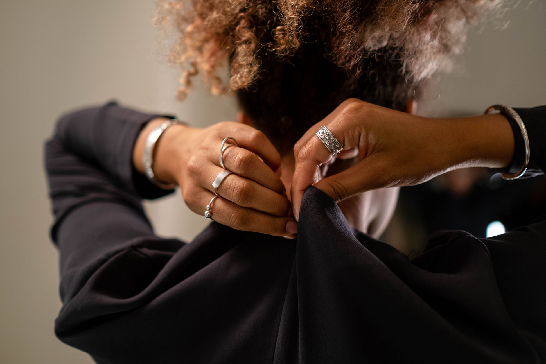 Close-up of a woman's hands fastening a zipper on a dress, showcasing jewelry.