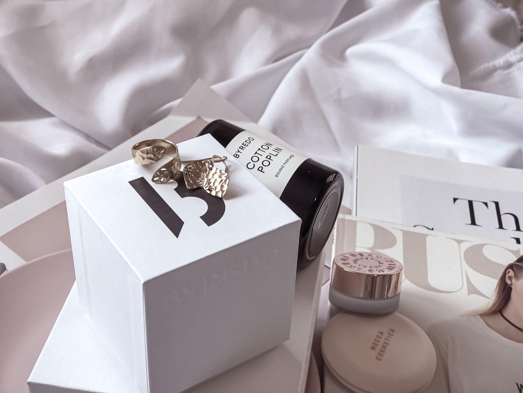 Stylish arrangement of luxury beauty items and jewelry on a white sheet setting.