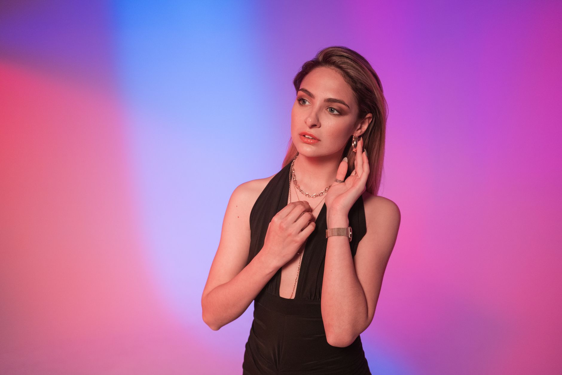 Fashionable woman in a black dress posing against a vibrant, colorful gradient background.