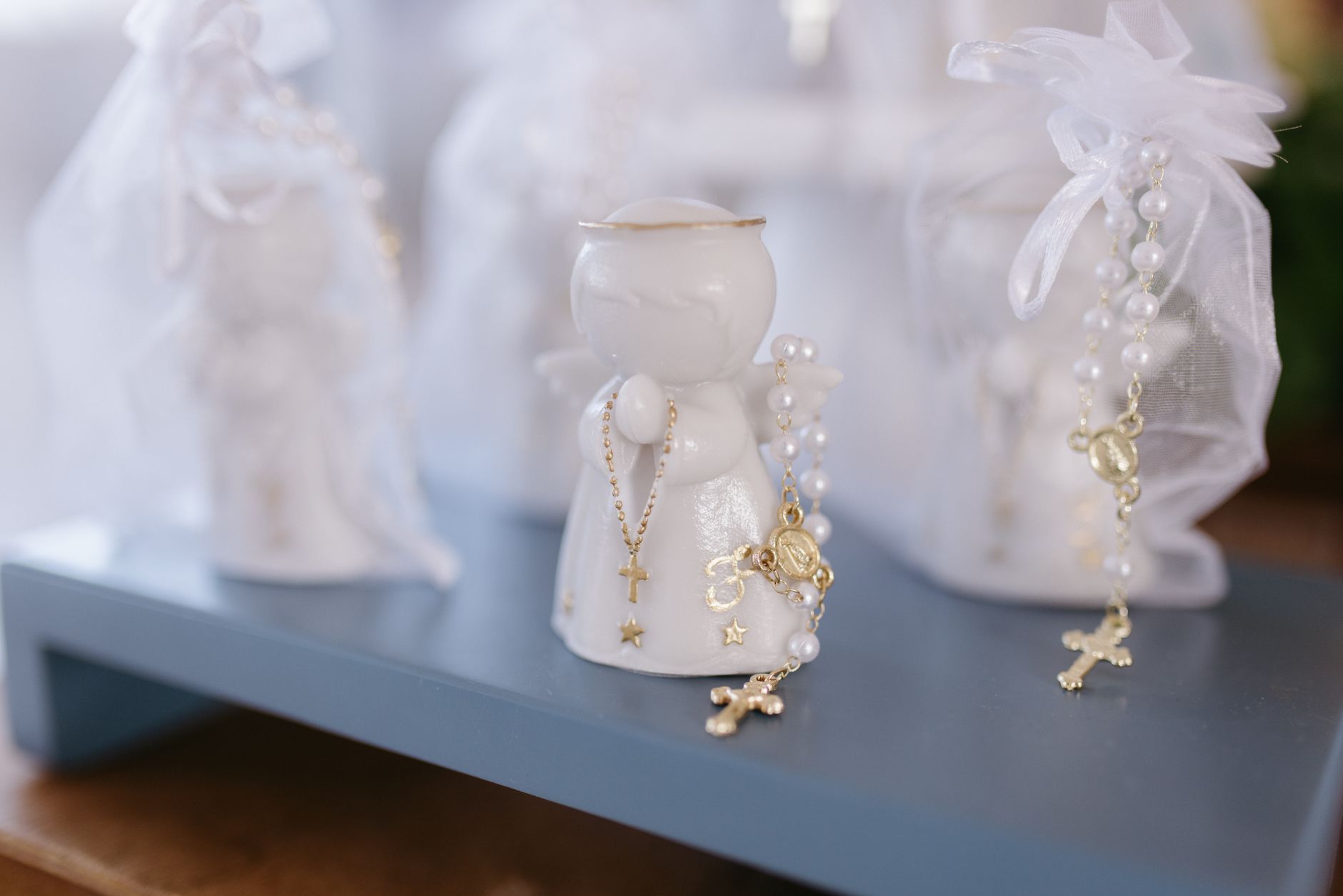 Delicate white ceramic angel figurine adorned with gold rosary beads on a display.