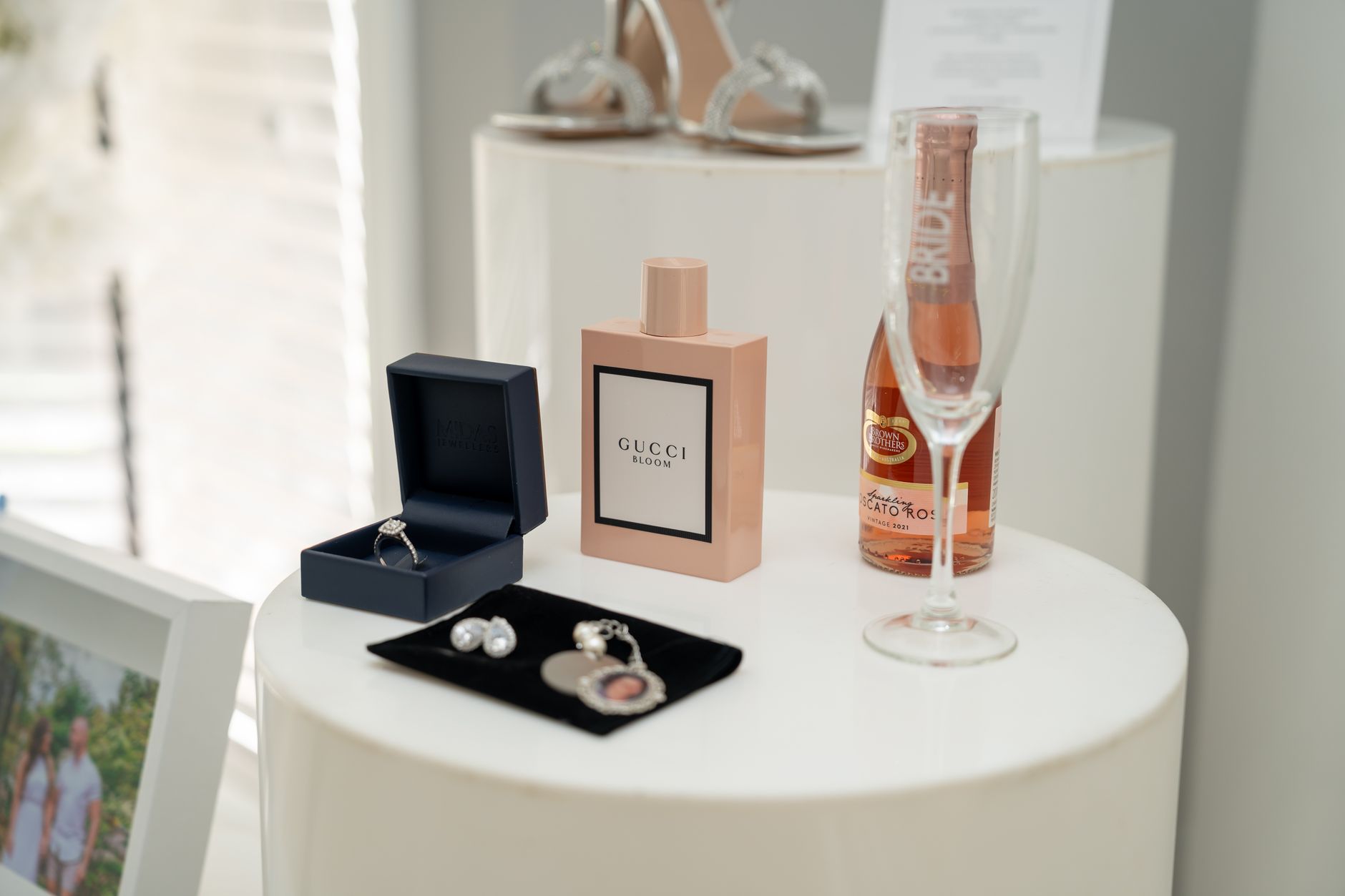 A collection of bridal accessories including perfume, jewelry, and champagne on a stylish table.