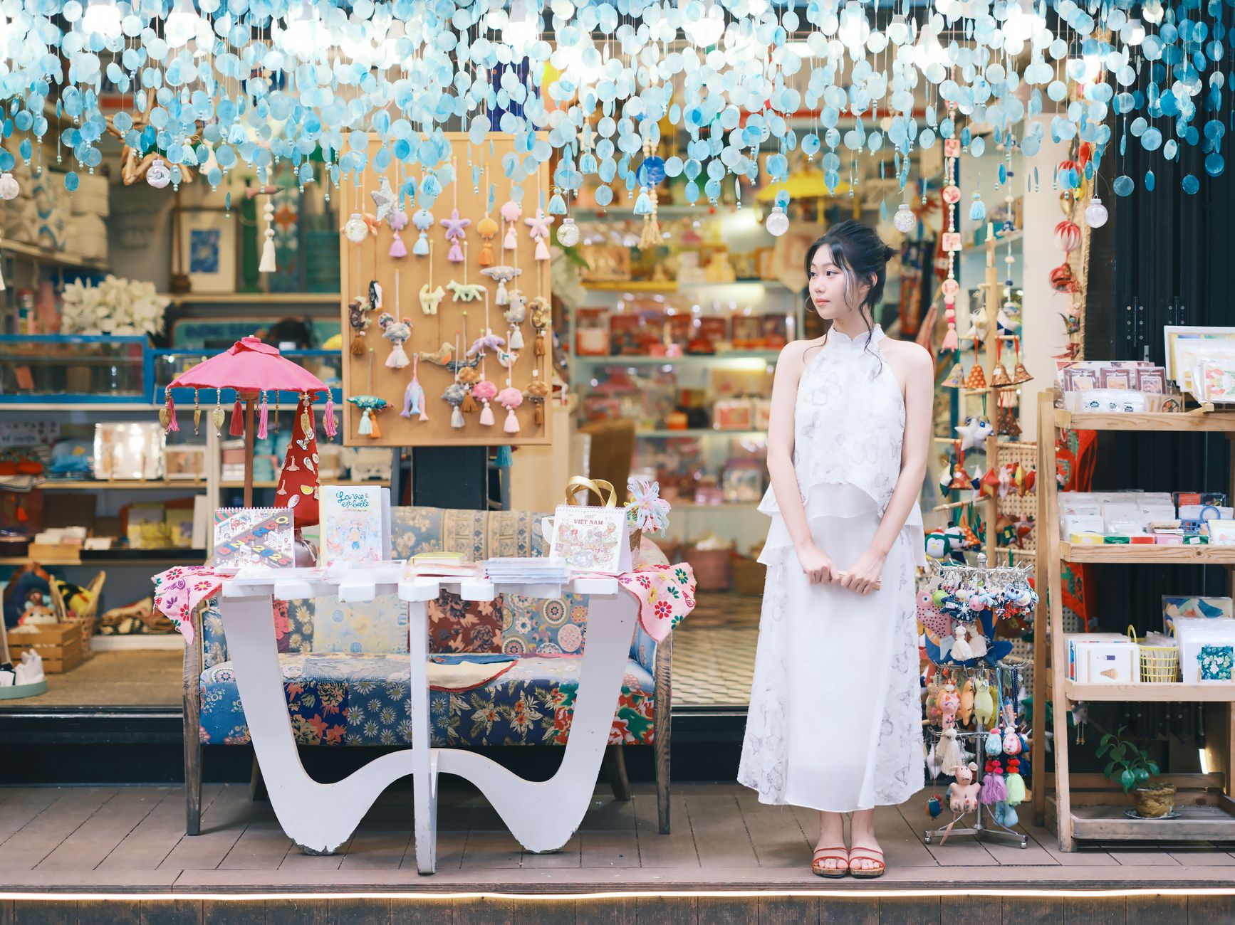 An elegant woman standing outside a colorful boutique adorned with hanging ornaments.
