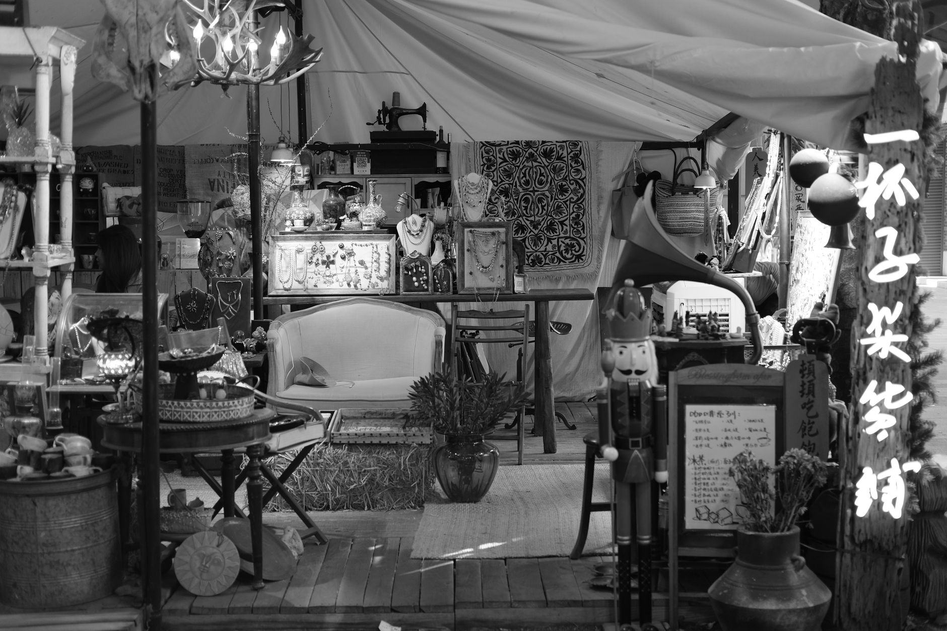 Black and white image of a vintage market stall filled with eclectic decor and jewelry.