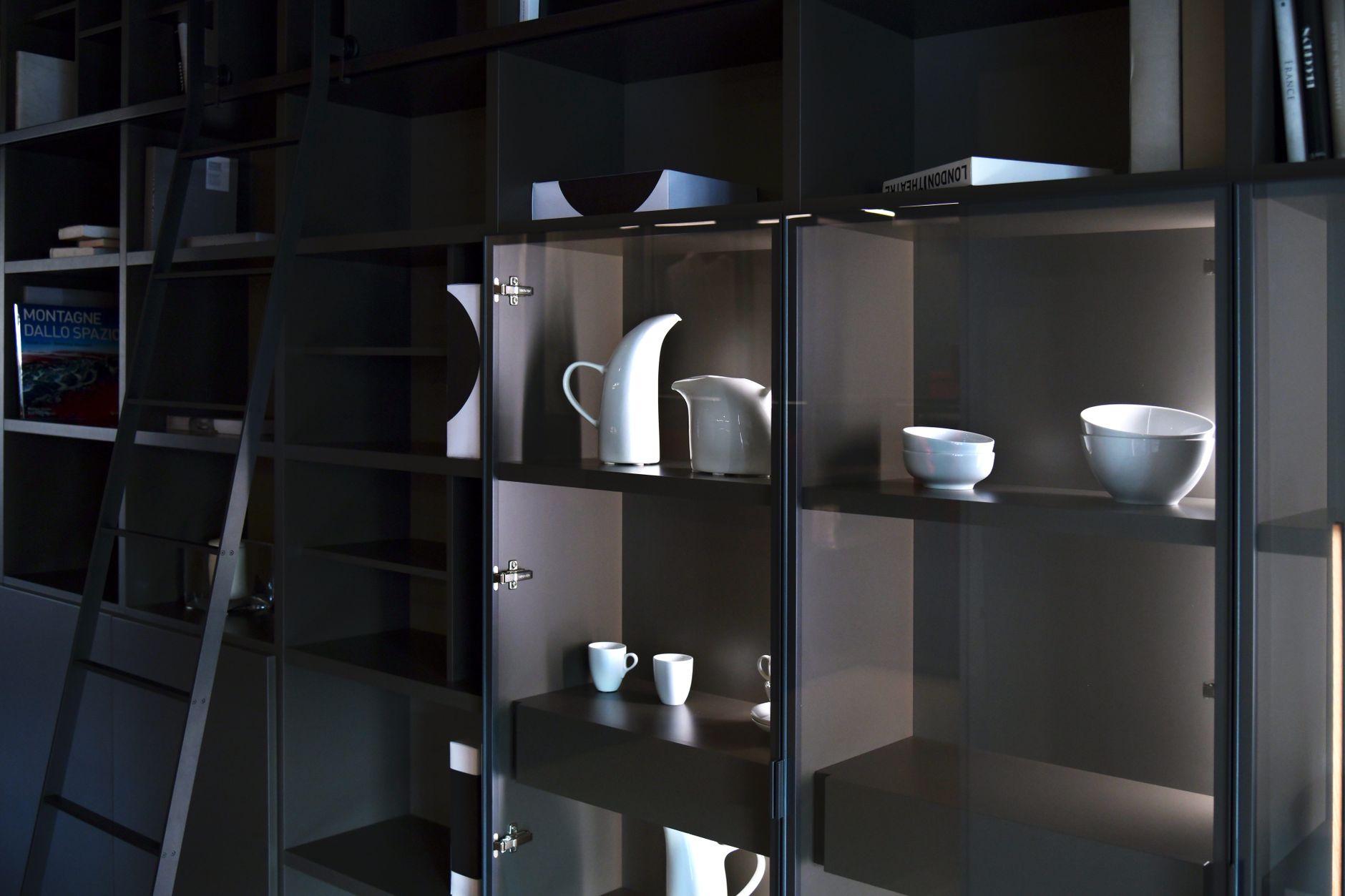 Stylish display of white ceramic tableware on dark shelving in contemporary setting.