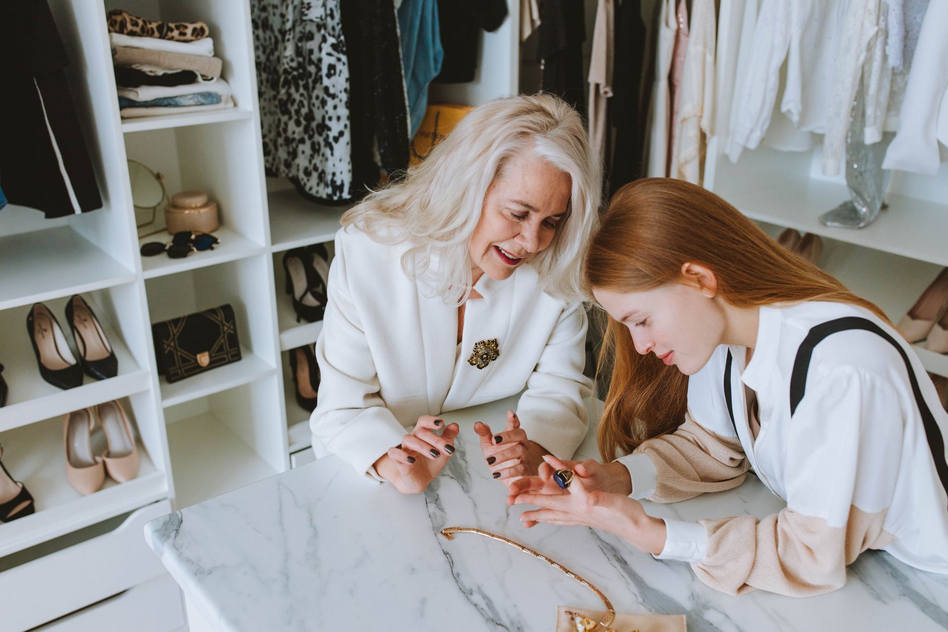 Two women exploring luxury jewelry in a stylish wardrobe setting.