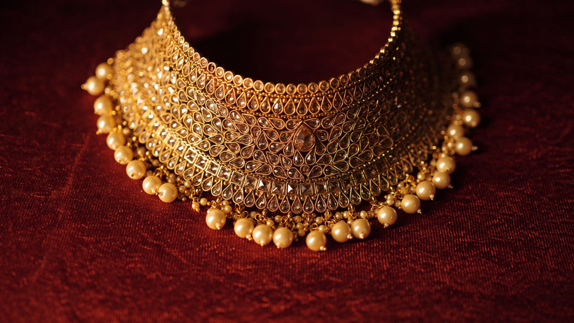 Elegant gold necklace with pearls on a rich red background, showcasing fine craftsmanship.