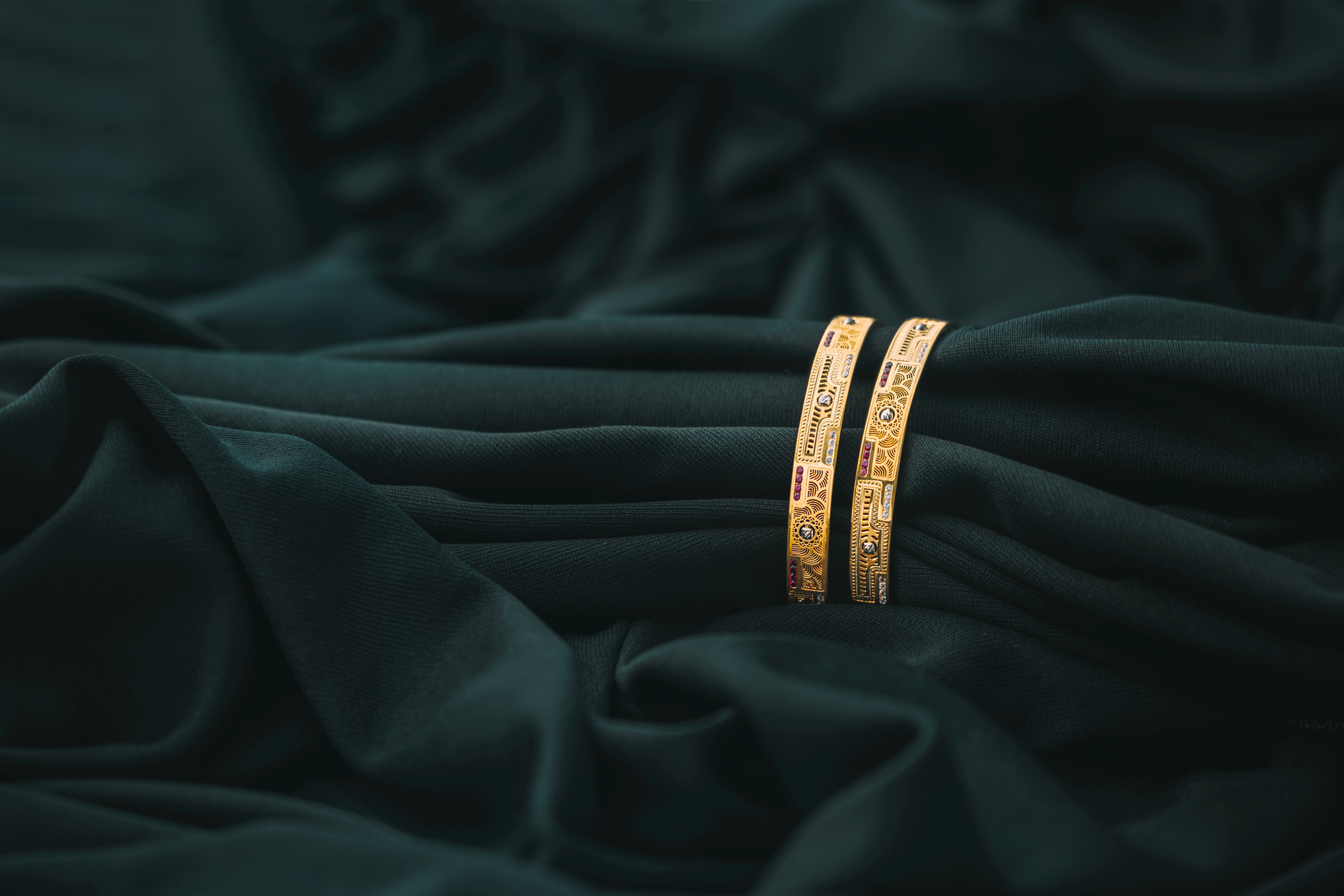 A pair of ornate golden bangles resting on rich, dark green fabric, creating a luxurious and elegant scene.