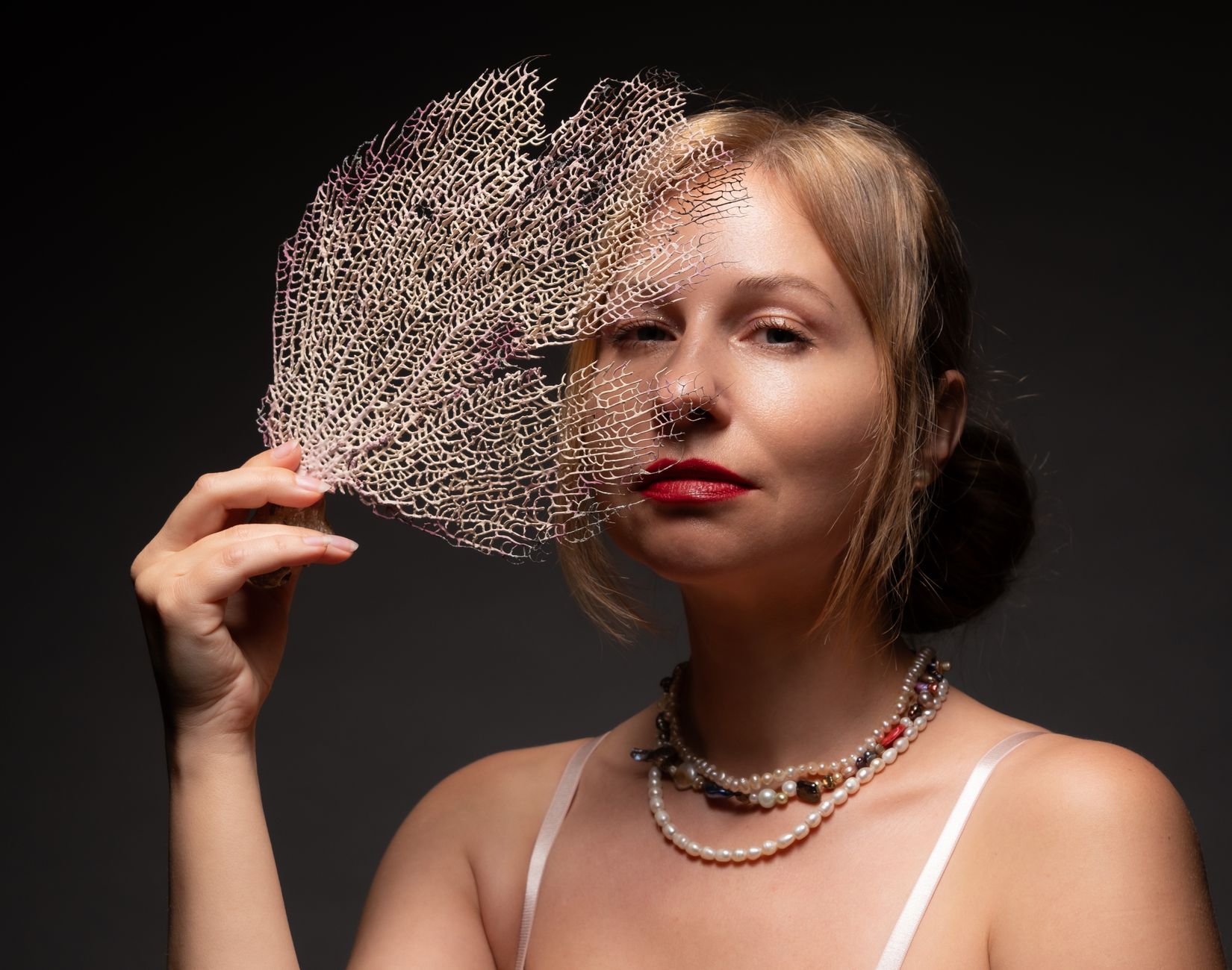 Stylish portrait of a woman holding a sea fan, creating an artistic blend of natural and human beauty.