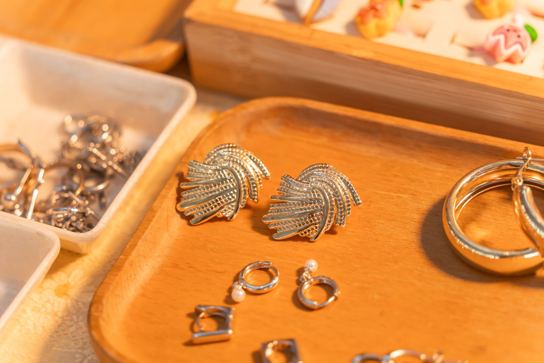 A close-up of elegant silver earrings and rings displayed on a wooden tray with warm lighting.