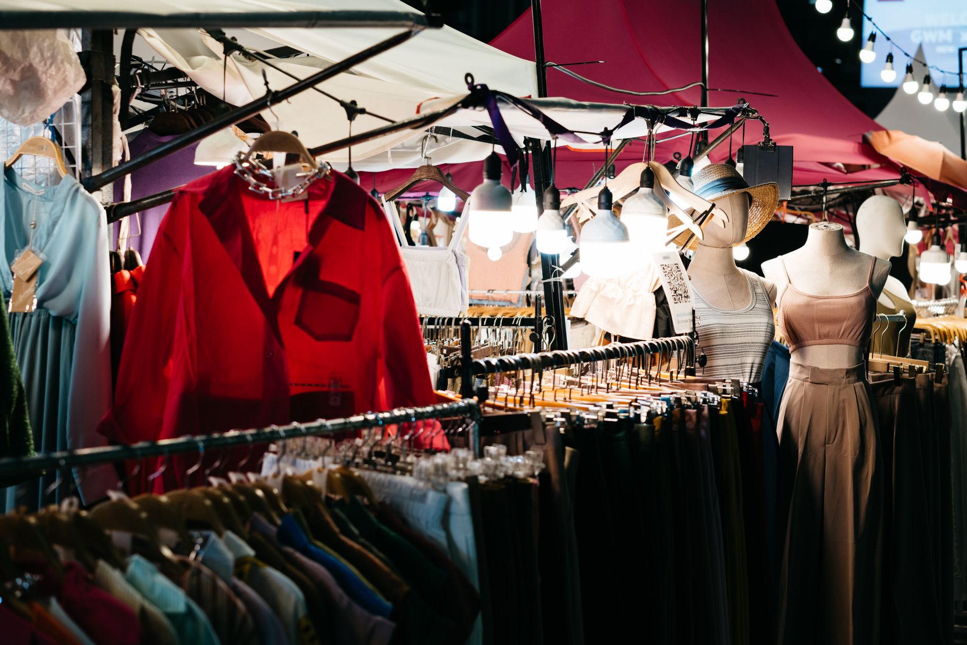 Colorful illuminated clothing stalls at a bustling outdoor night market.