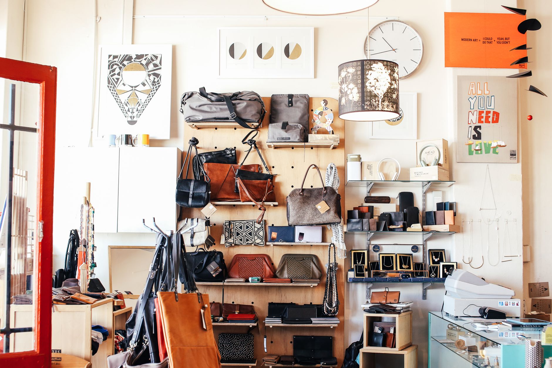 Abundance of stylish bags placed on shelves near wall with various goods and decorations in modern light shop with cashbox