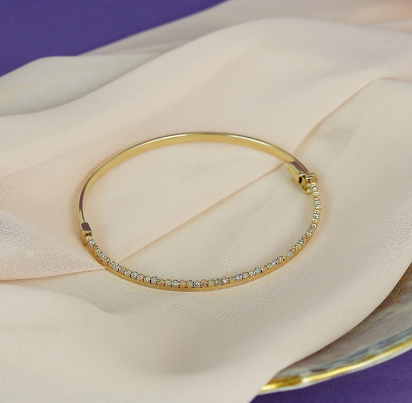 A close-up of a gold bracelet adorned with diamonds, elegantly displayed on soft fabric.