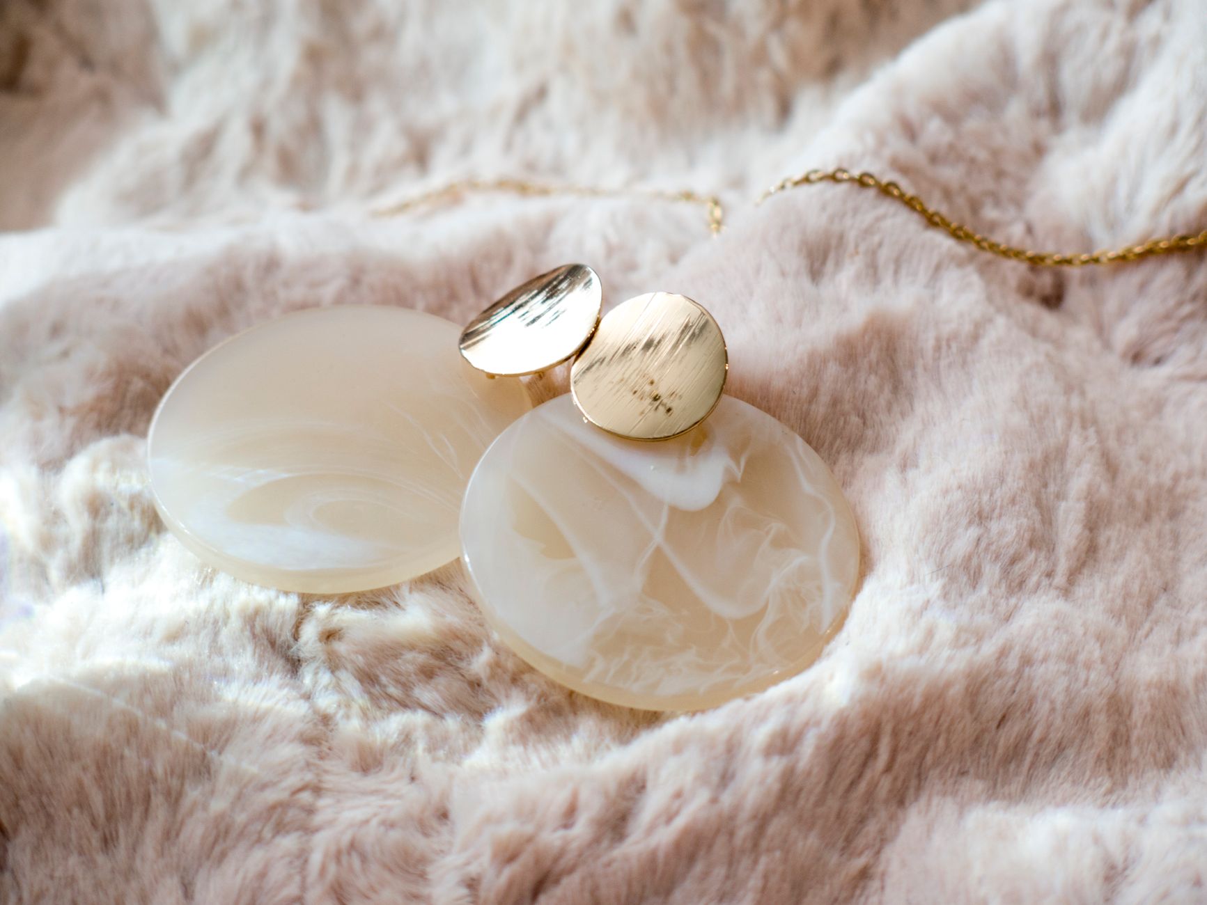 Close-up of elegant marble earrings with gold accents displayed on soft fabric for a luxurious look.