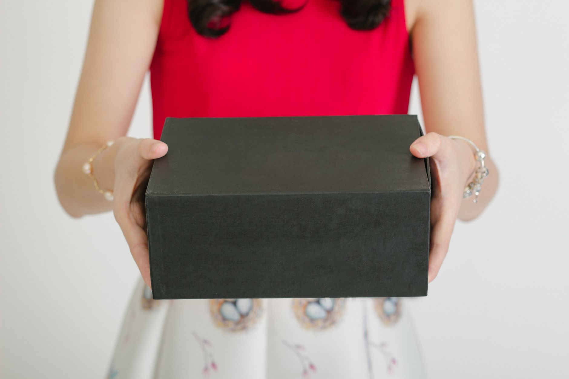 Woman holding a black gift box in a red top, showcasing elegance and surprise.