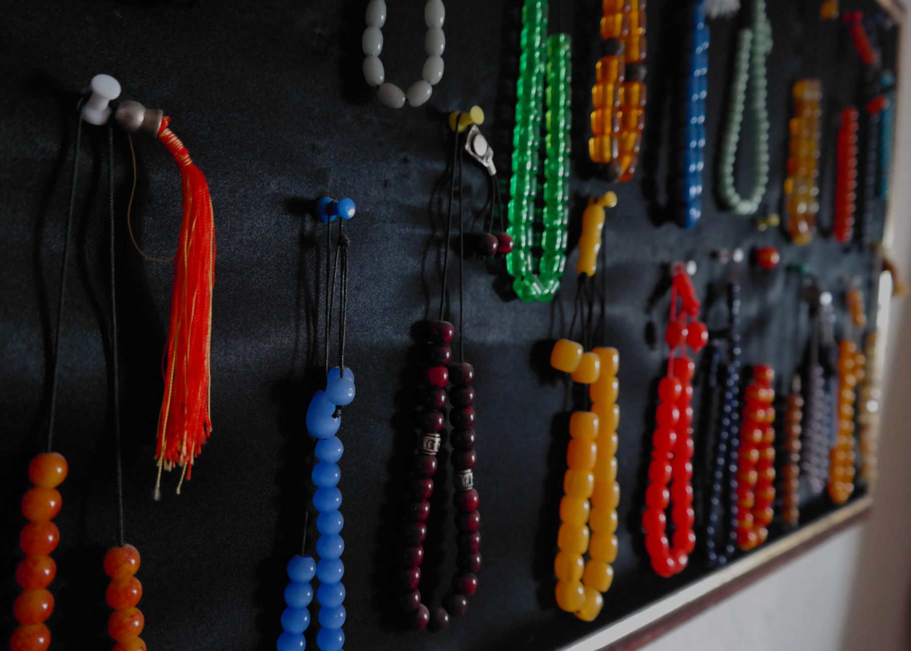 Close-up of various colorful beaded necklaces hanging against a dark background.