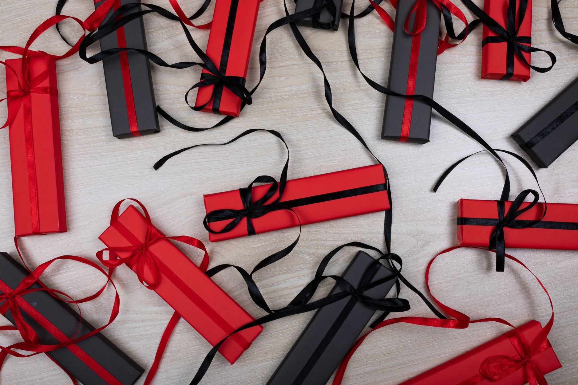 Top view of stylish gift boxes wrapped with red and black ribbons on a wooden surface.