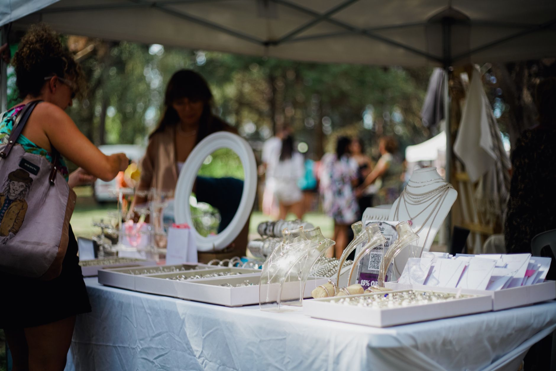 Outdoor jewelry market scene with diverse people browsing various stalls under a tent.