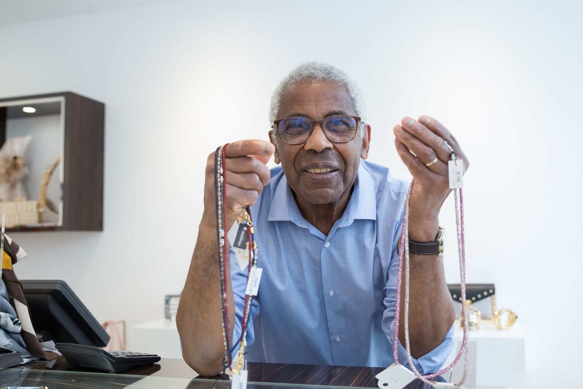 Senior man smiling and showcasing necklaces in a bright, modern store.