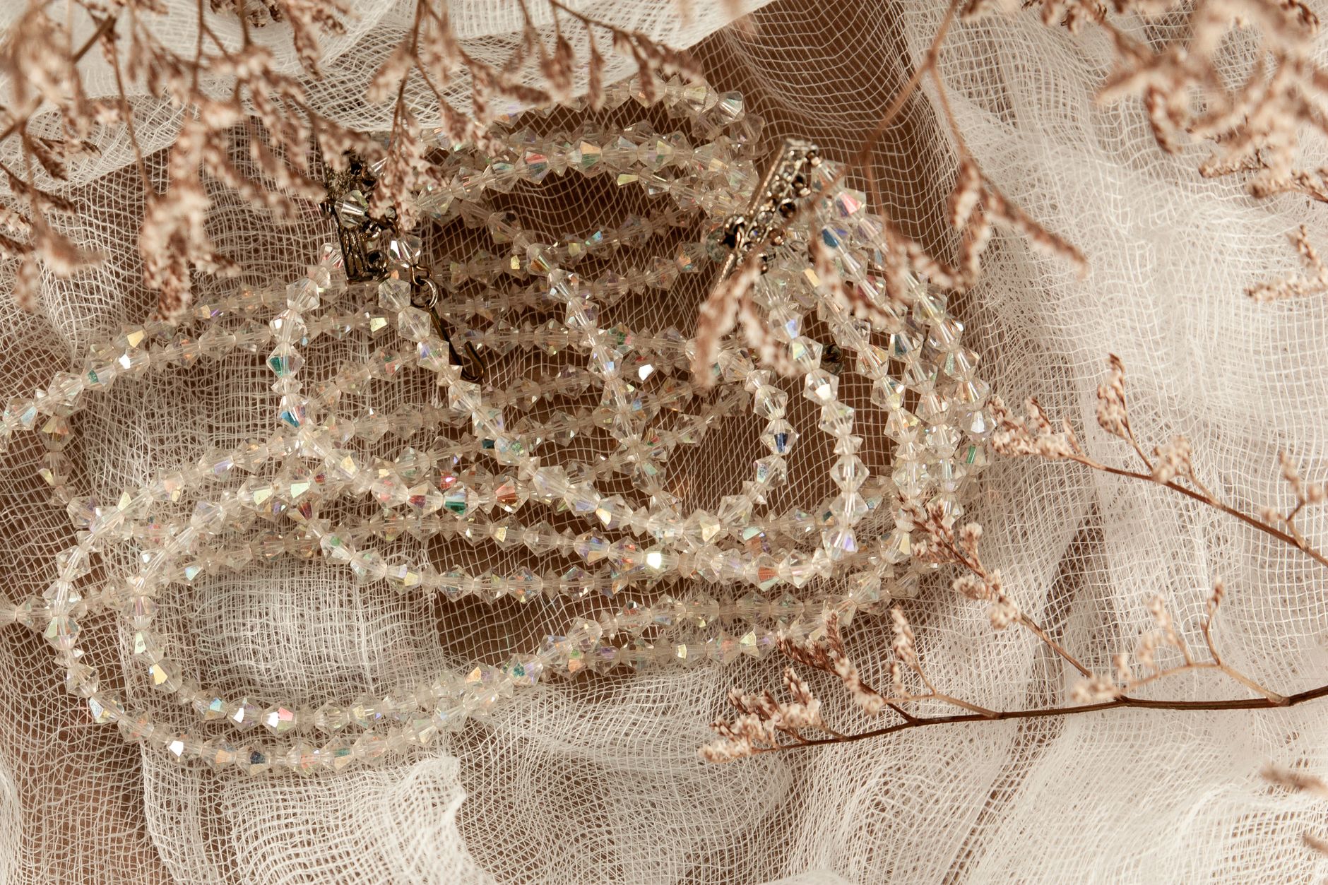 A sparkling crystal necklace elegantly arranged on delicate lace fabric with dried floral accents.