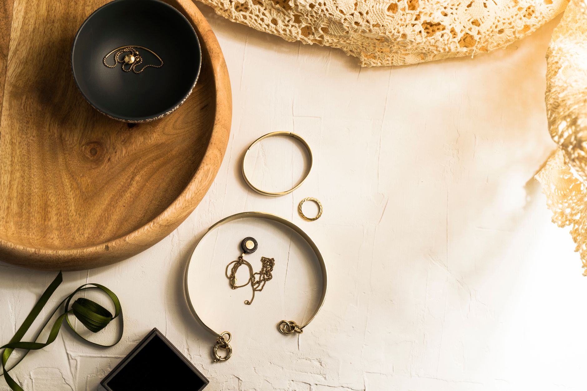 Elegant display of gold jewelry on a wooden tray with top view on a white surface.