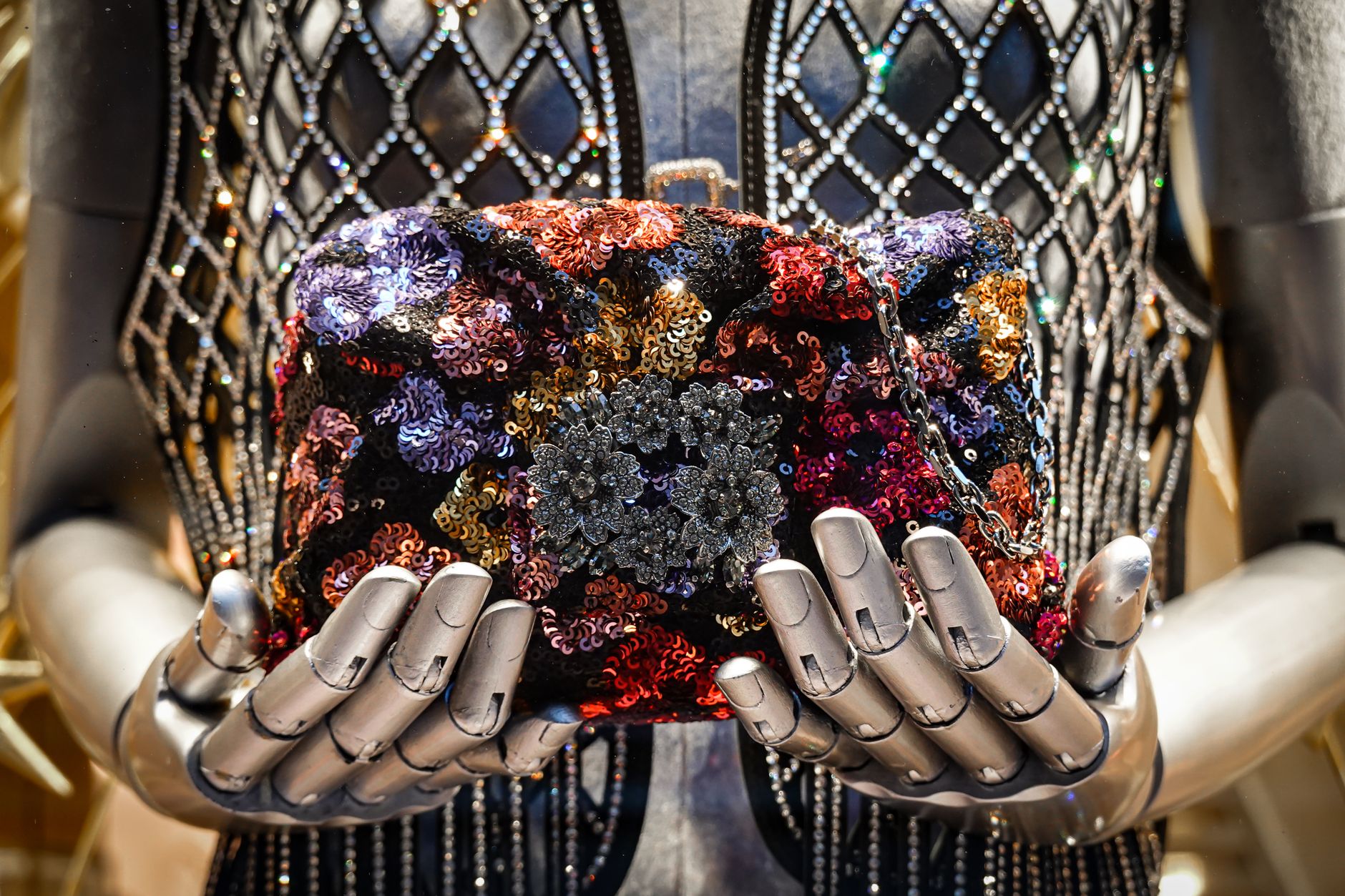 A fashion mannequin showcases a colorful sequin handbag held gracefully by robotic hands.
