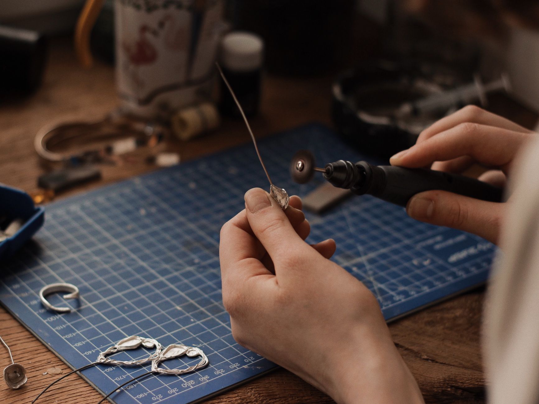 Close-up of a jeweler polishing silver earrings at a workbench using precision tools.