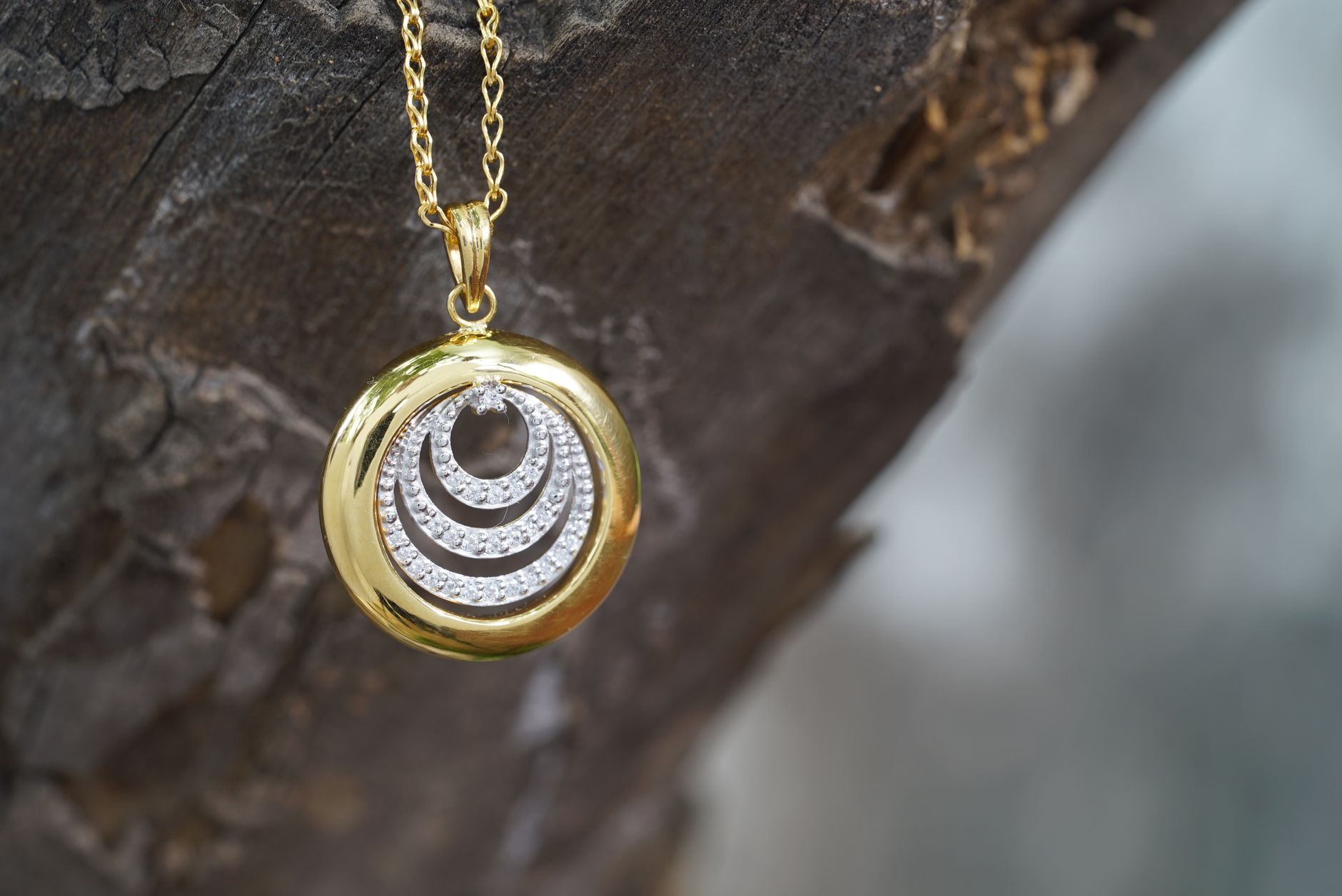 Round golden chain with pendant with small crystals hanging on tree trunk on blurred background