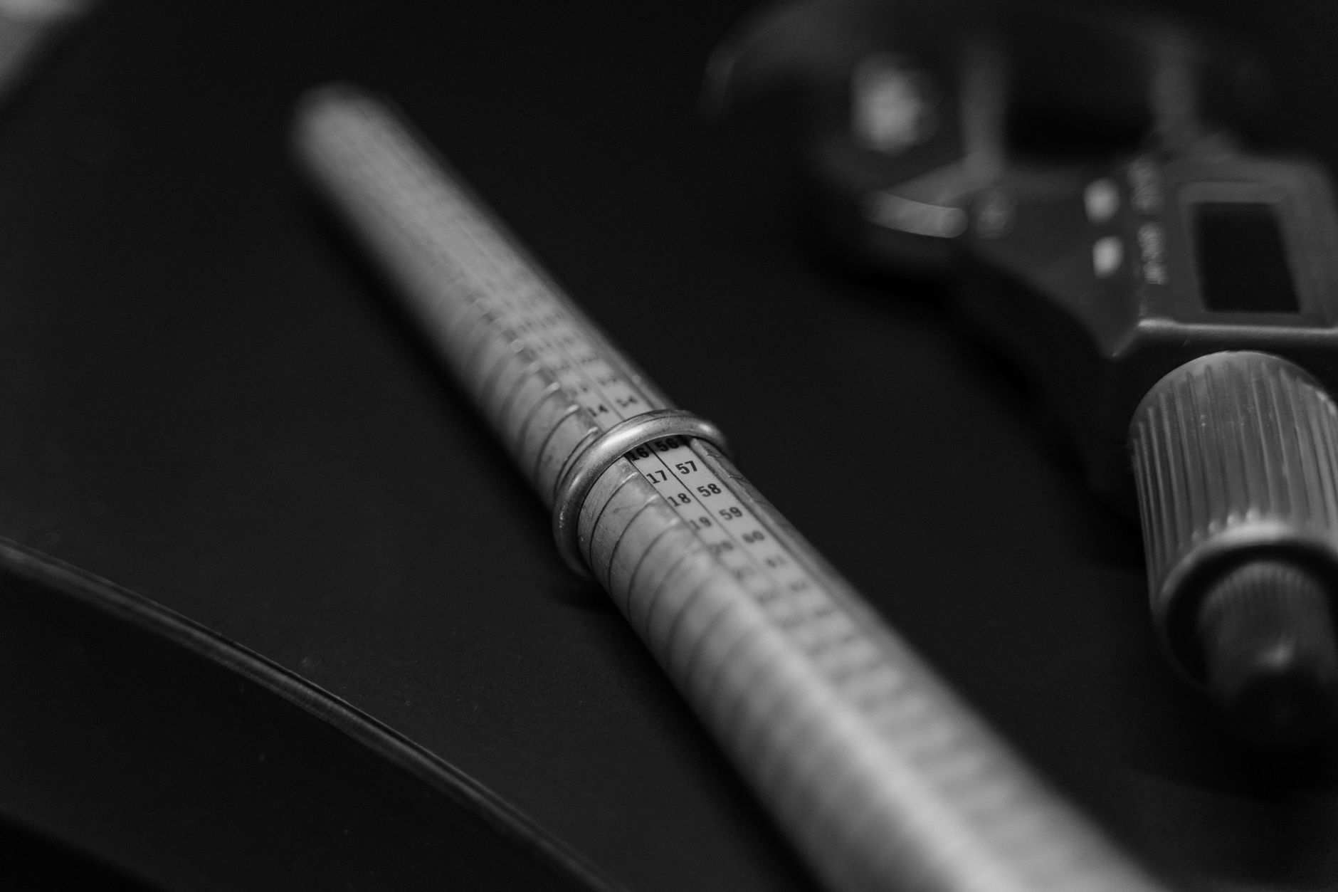 Black and white image showing a focus on jewelry measuring tools on a workbench.