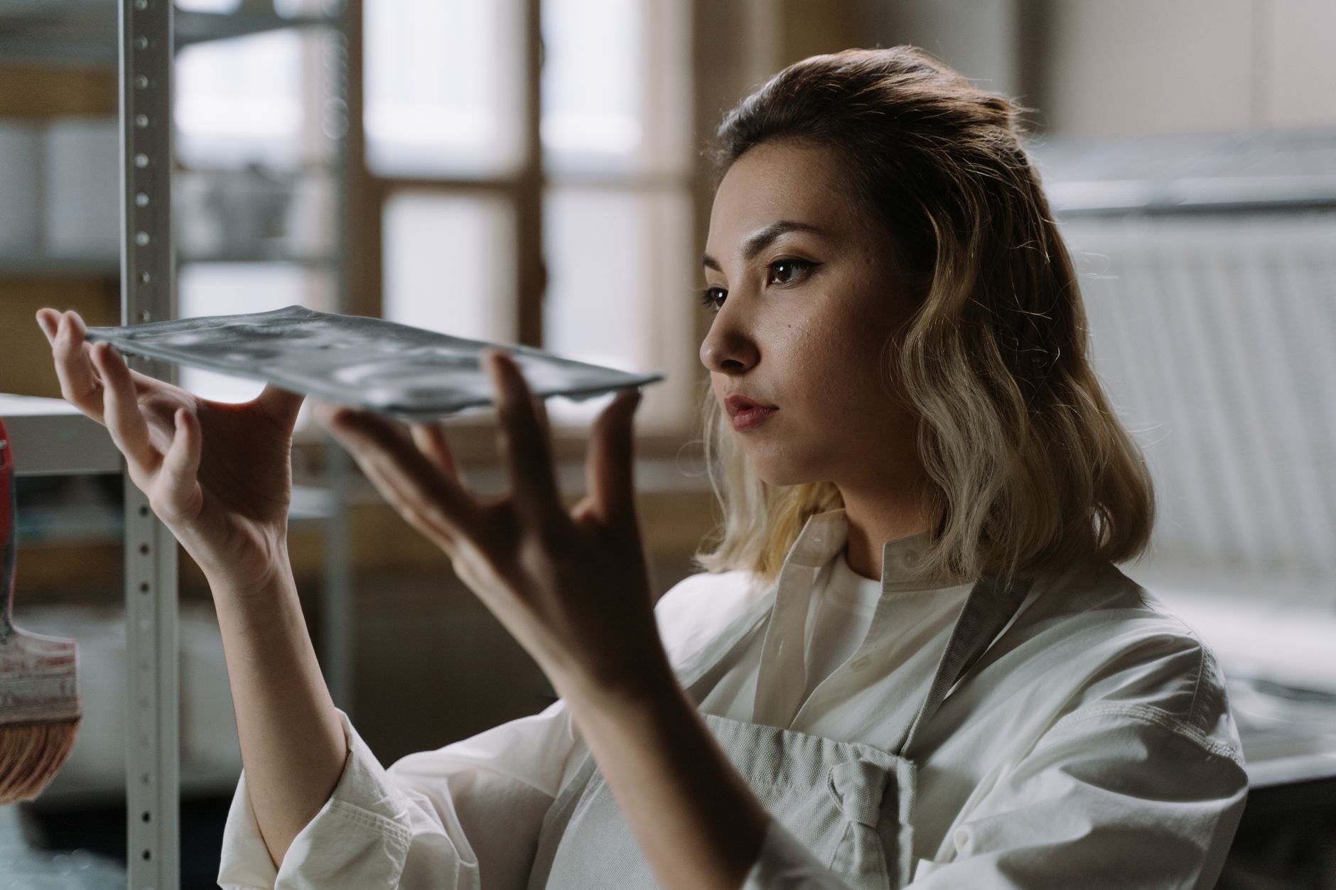 Female artisan carefully examining handcrafted glassware in a well-lit workshop setting.