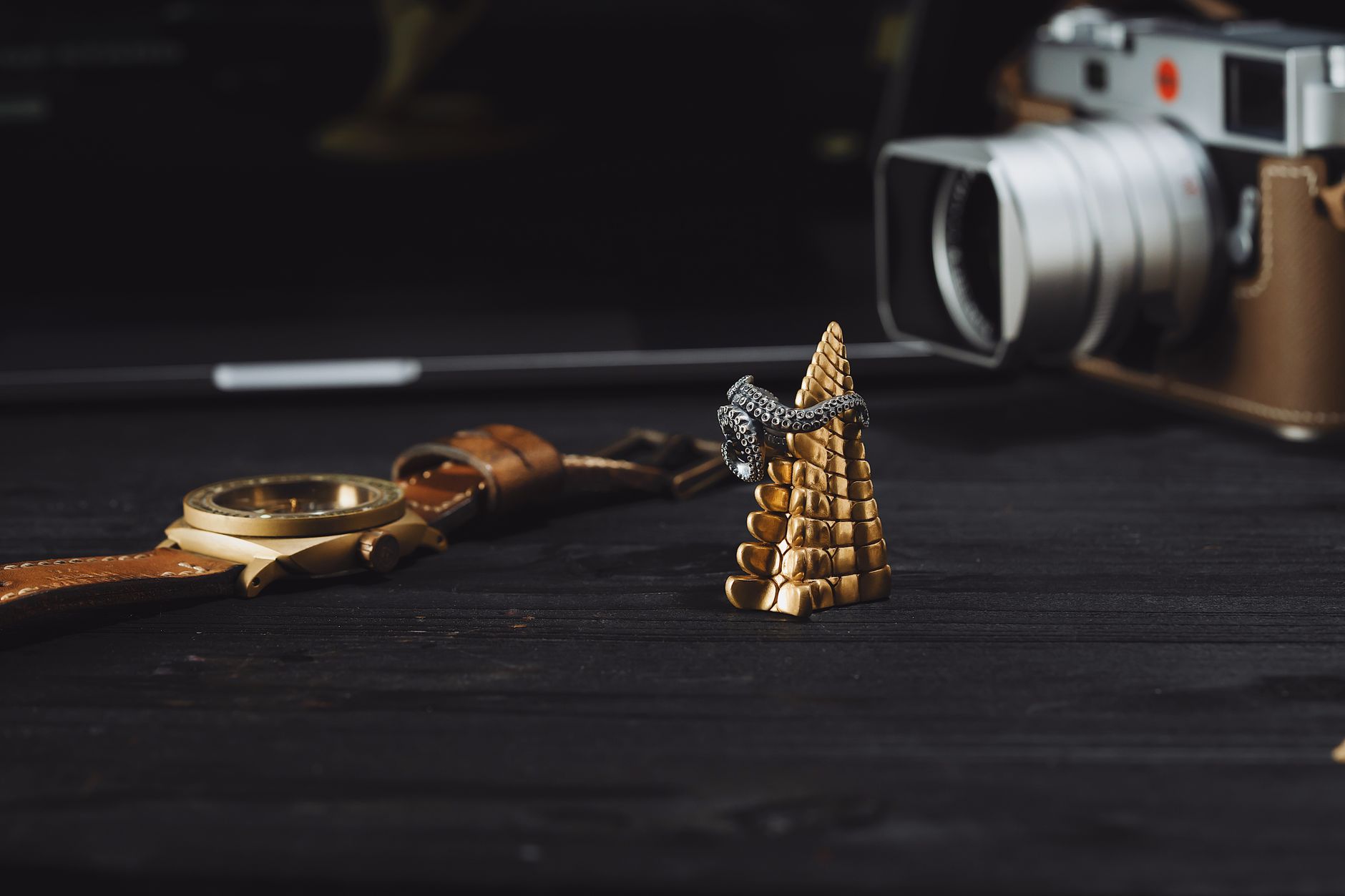 Stylish arrangement featuring a golden wristwatch, a ring on gold cone stand, and a camera in the background.