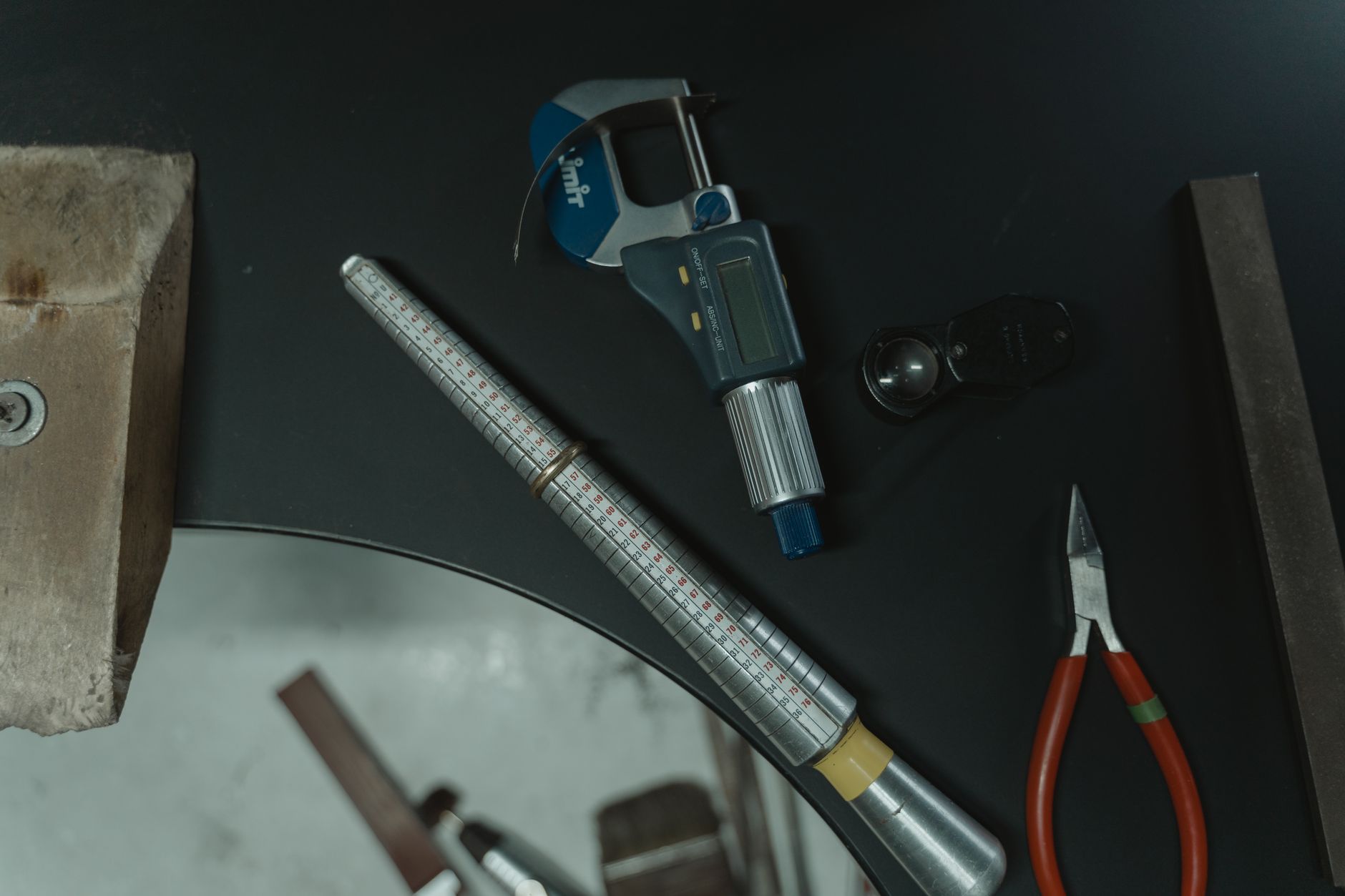 A collection of jewelry crafting tools including a ring mandrel and caliper on a workbench.