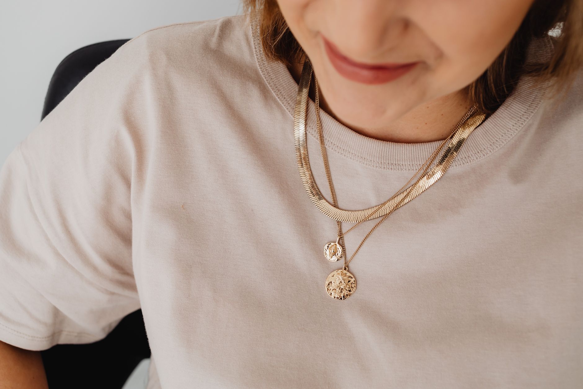Close-up view of a woman wearing layered gold necklaces, smiling softly.