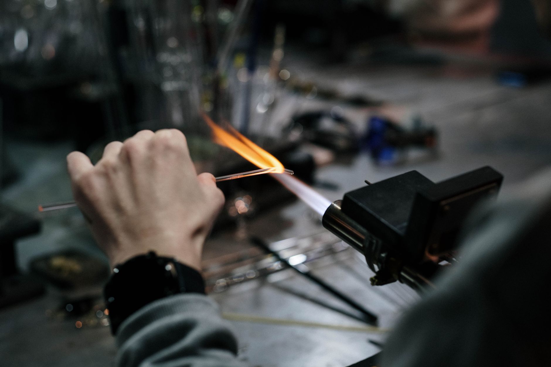 Close-up of a glass blower shaping glass with precision while using a blowtorch in a workshop.