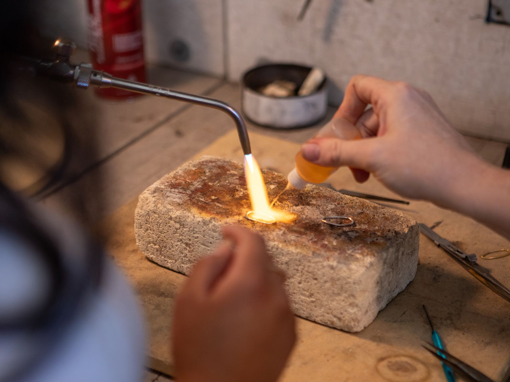 A jewelry artisan uses a blowtorch to craft a ring in a workshop setting.
