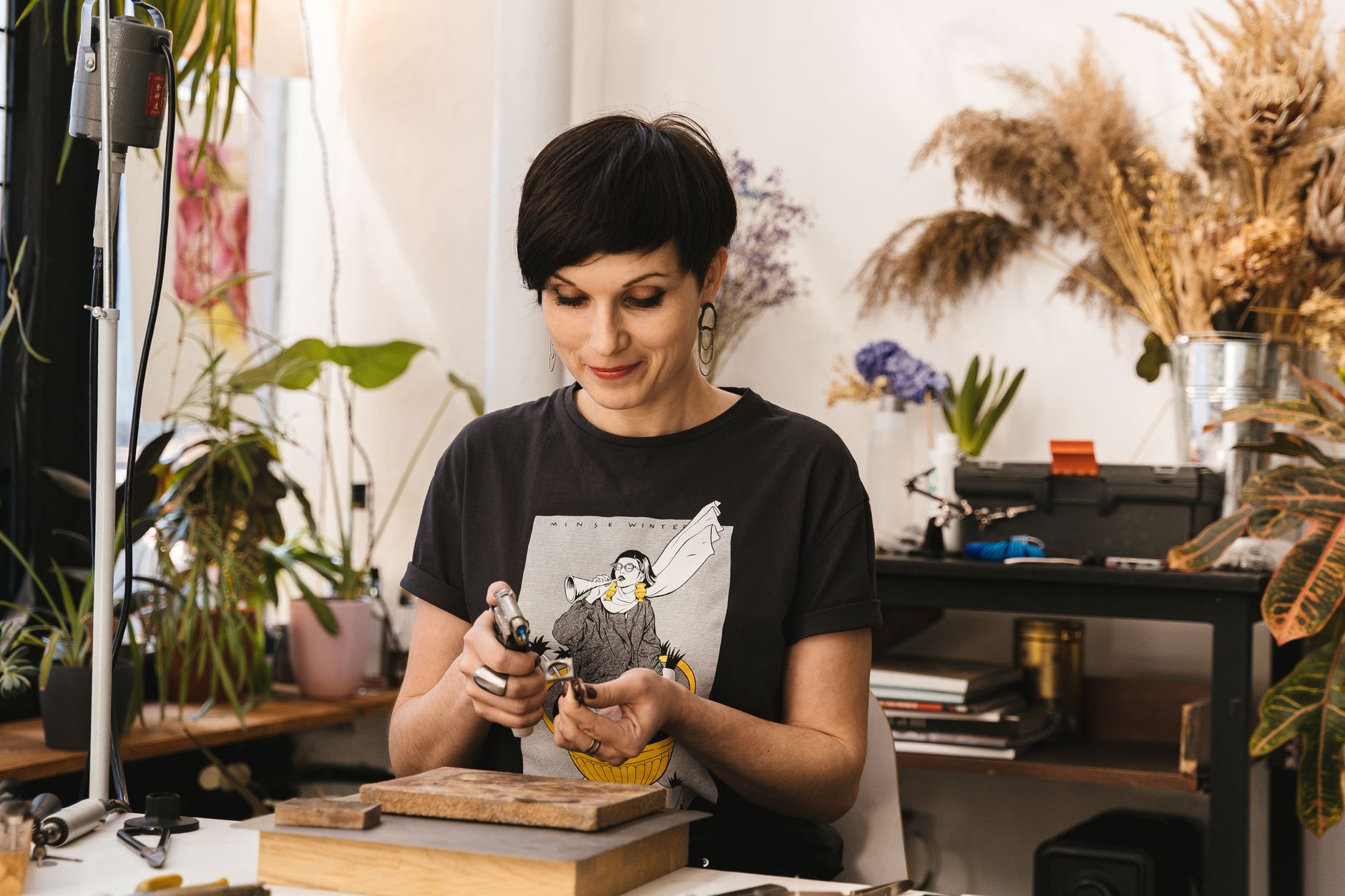 A female artisan using tools in her vibrant, plant-filled workshop.