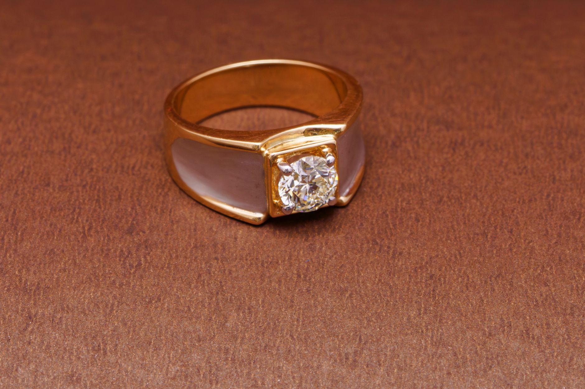 Close-up of a gold ring featuring a diamond, set against a warm brown background.