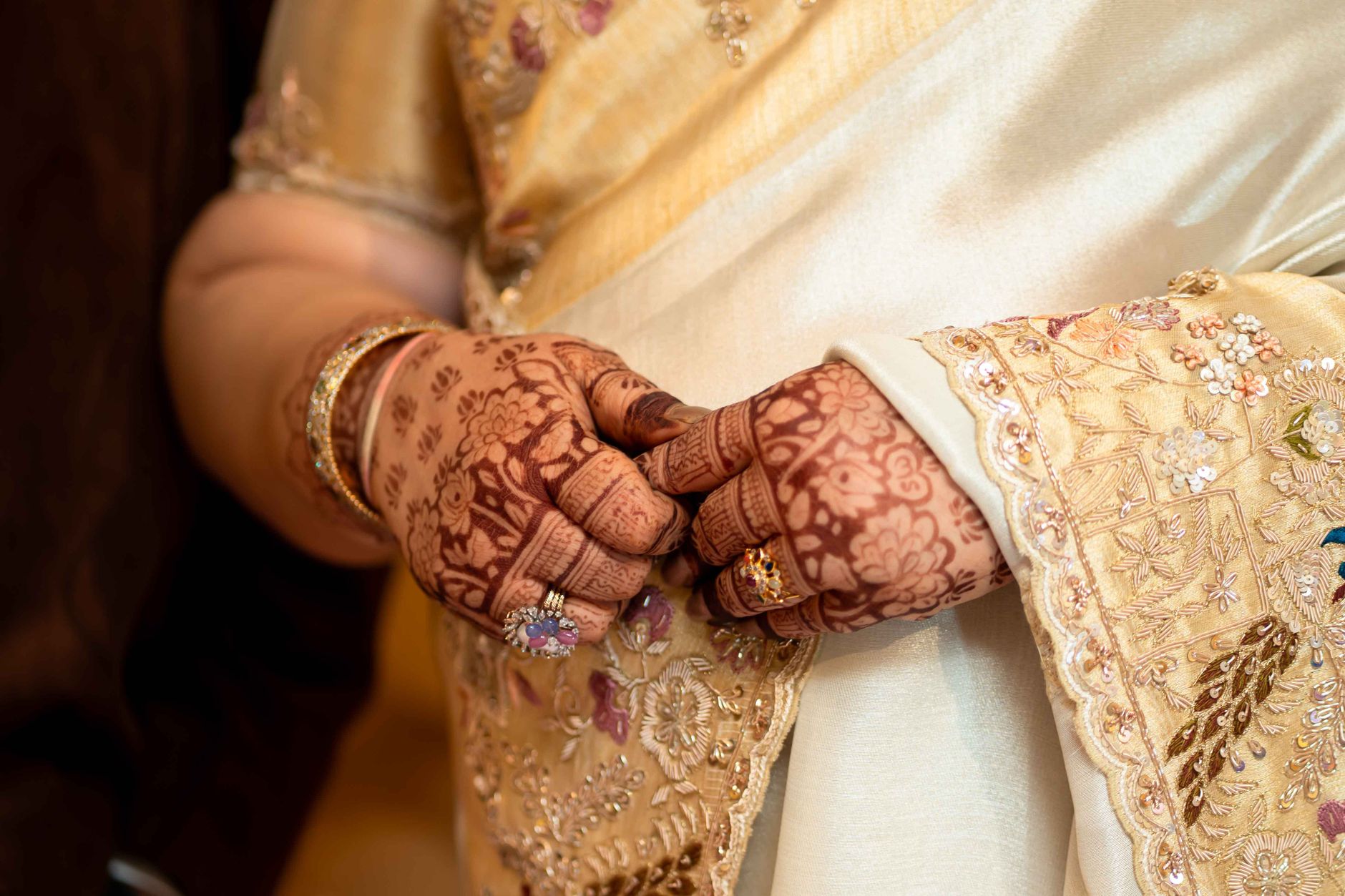 Close-up of a bride's hands with intricate henna and gold jewelry in a traditional saree.