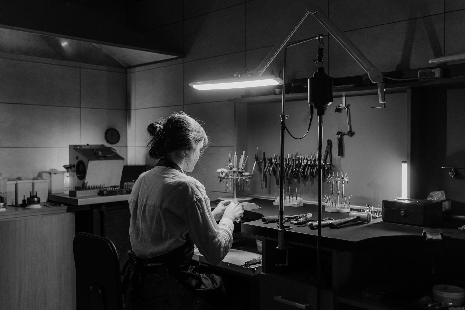 A woman working diligently in a dimly lit workshop, surrounded by tools.