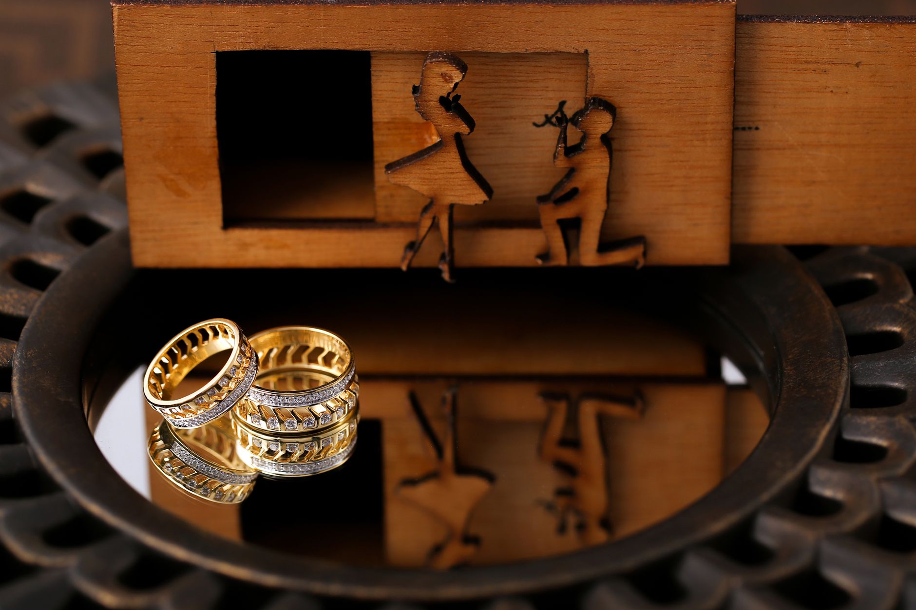 Gold wedding rings reflected with romantic wooden carvings in a detailed close-up shot.
