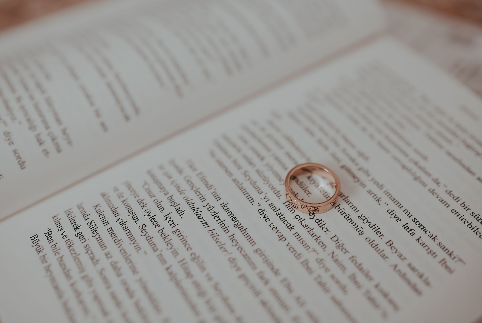 An elegant close-up of a wedding ring resting on an open book, casting a heart-shaped shadow.