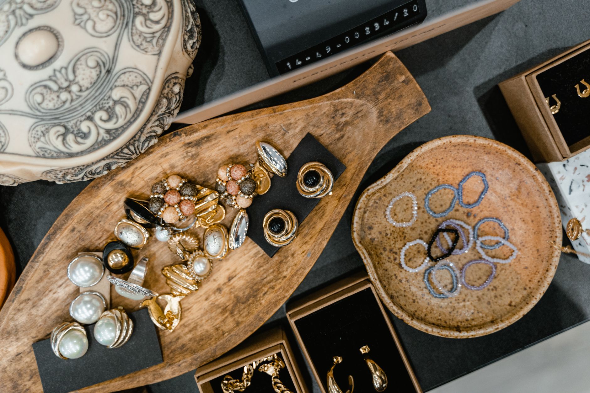 A top view of assorted jewelry including rings and bracelets in a wooden tray and ceramic dish.