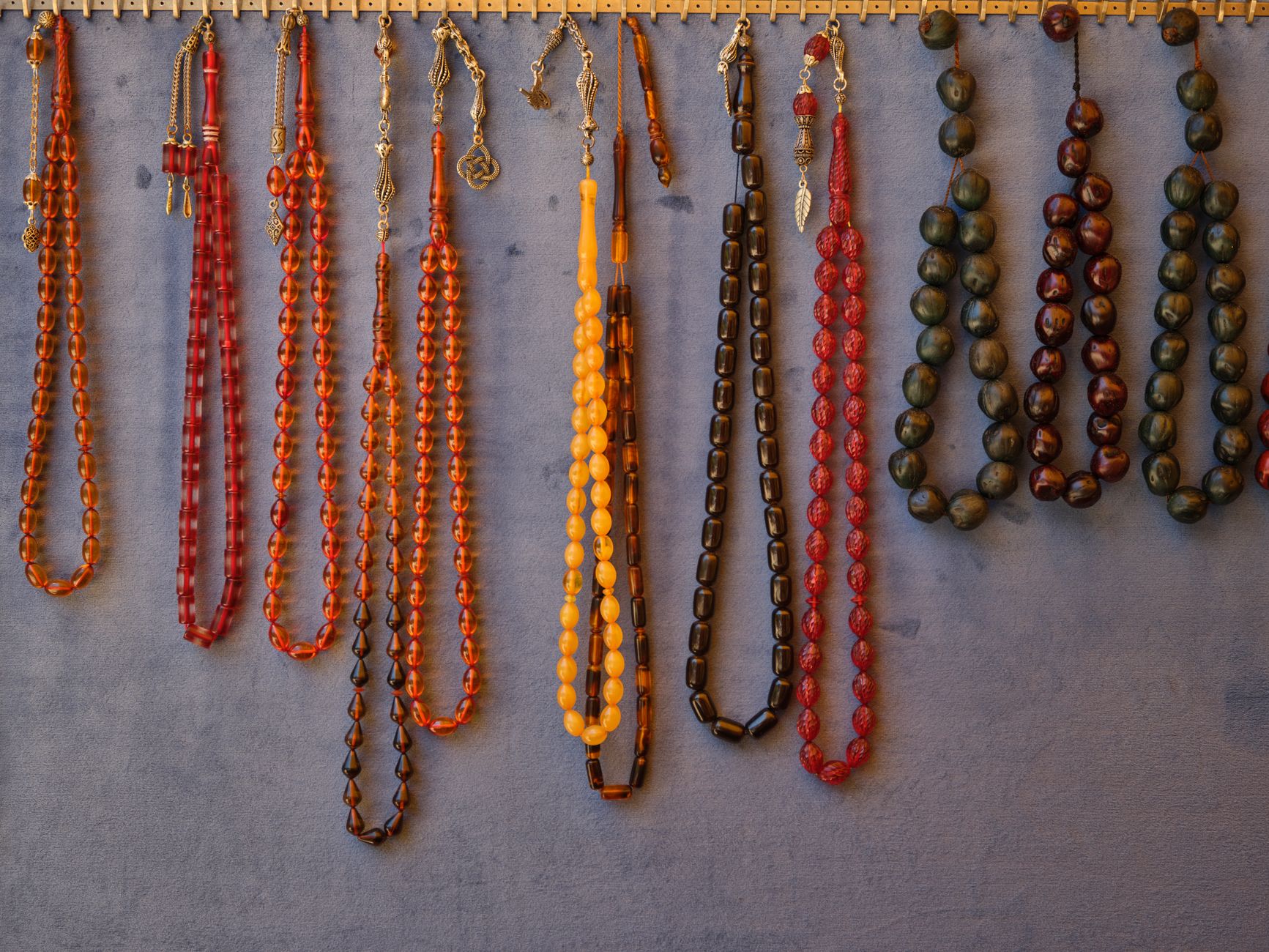 Collection of vibrant beaded necklaces hanging neatly on a gray wall.