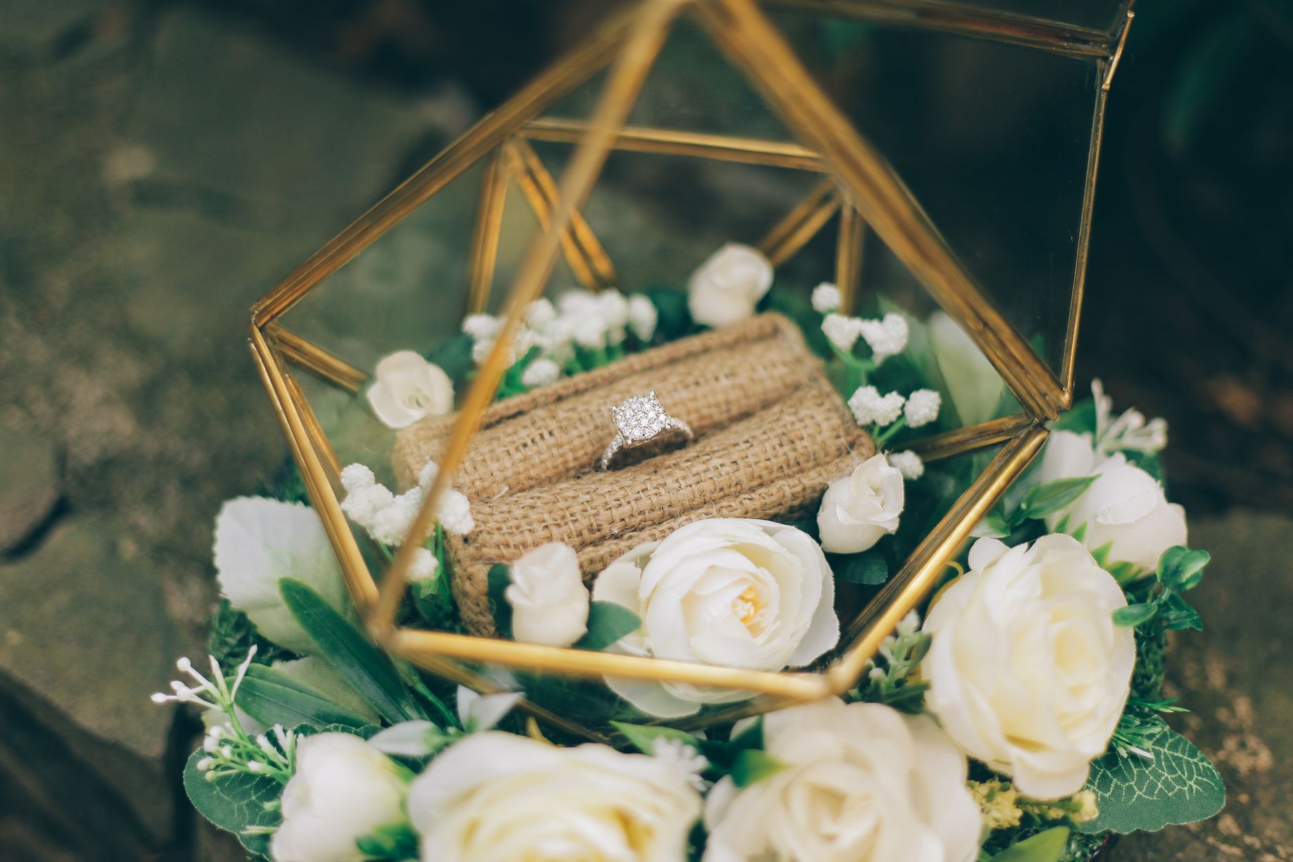 Close-up of a diamond ring in a geometric case surrounded by white roses.
