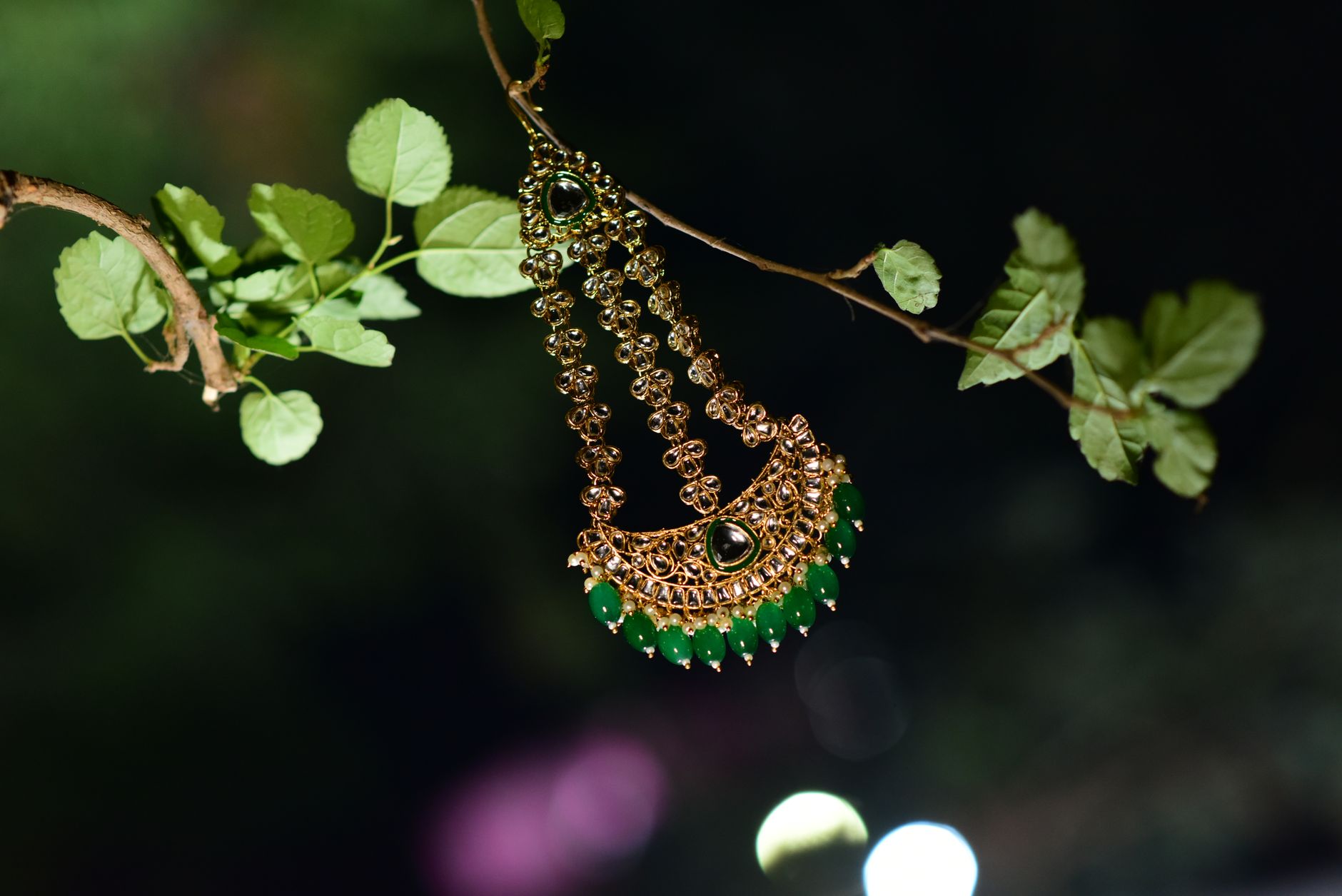 Intricate gold necklace with green gemstones hanging on a tree branch, emphasizing traditional Indian craftsmanship.