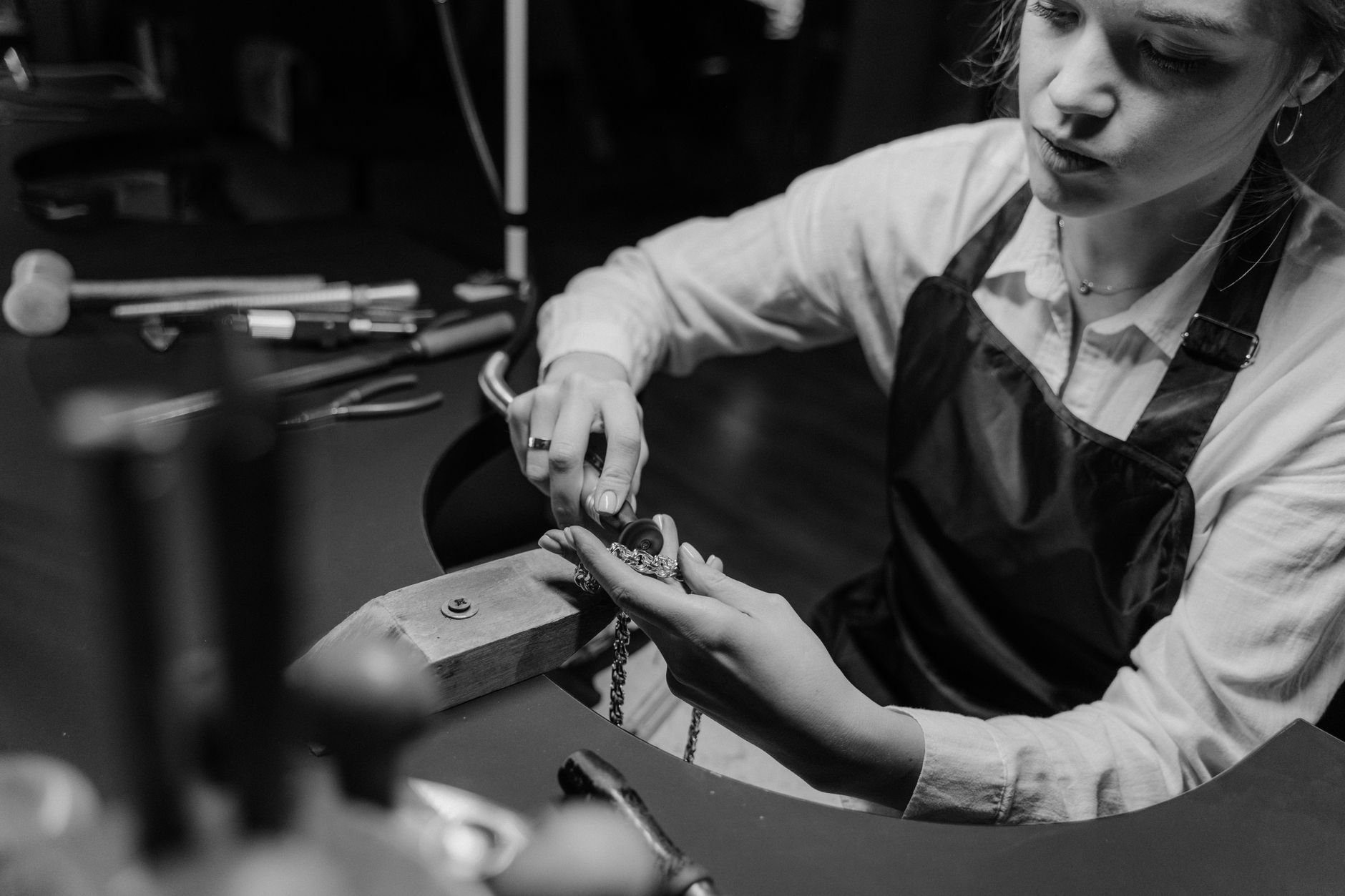 A jeweler meticulously working on a necklace with precision tools in a workshop setting.